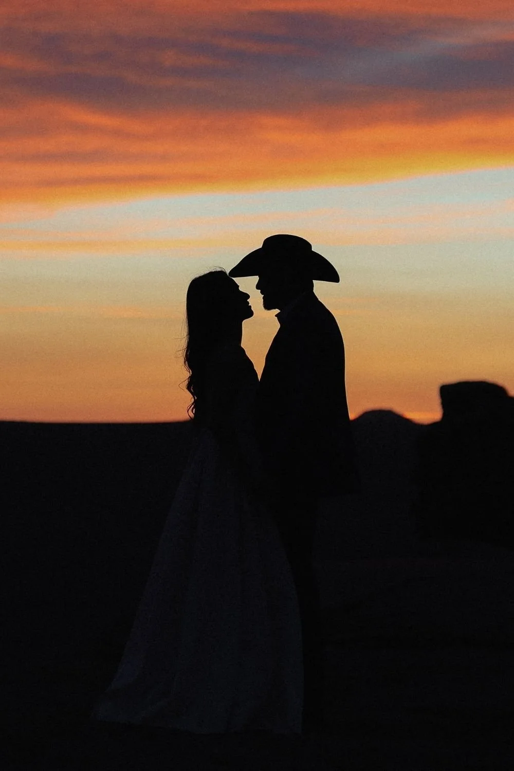 bride and groom silhouette in front of bright orange and blue Moab sunset.