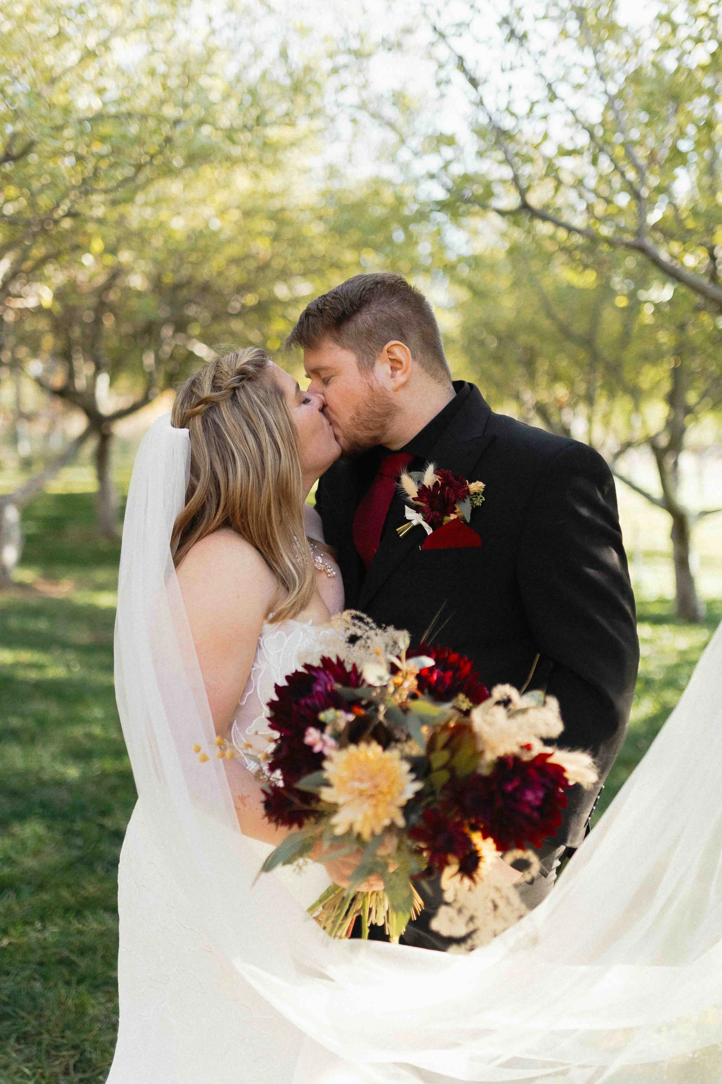 Bride and groom kissing in a green orchard.