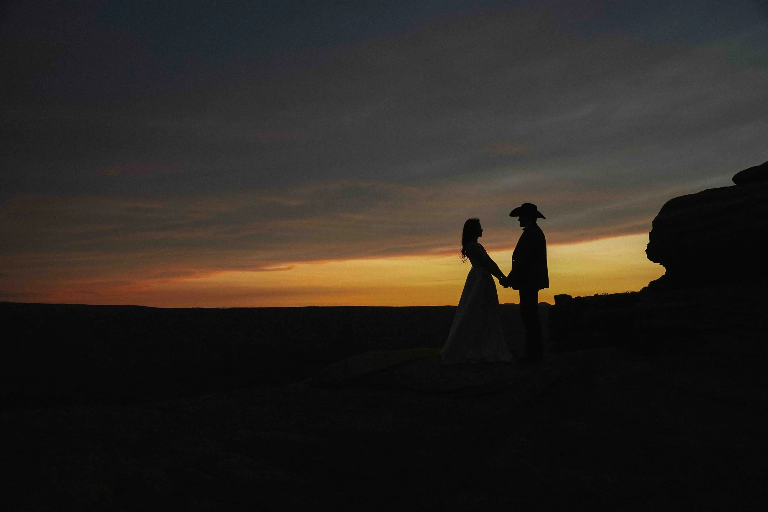 Silhouette of bride and groom holding hands in the desert sunset of yellow, blue and orange.