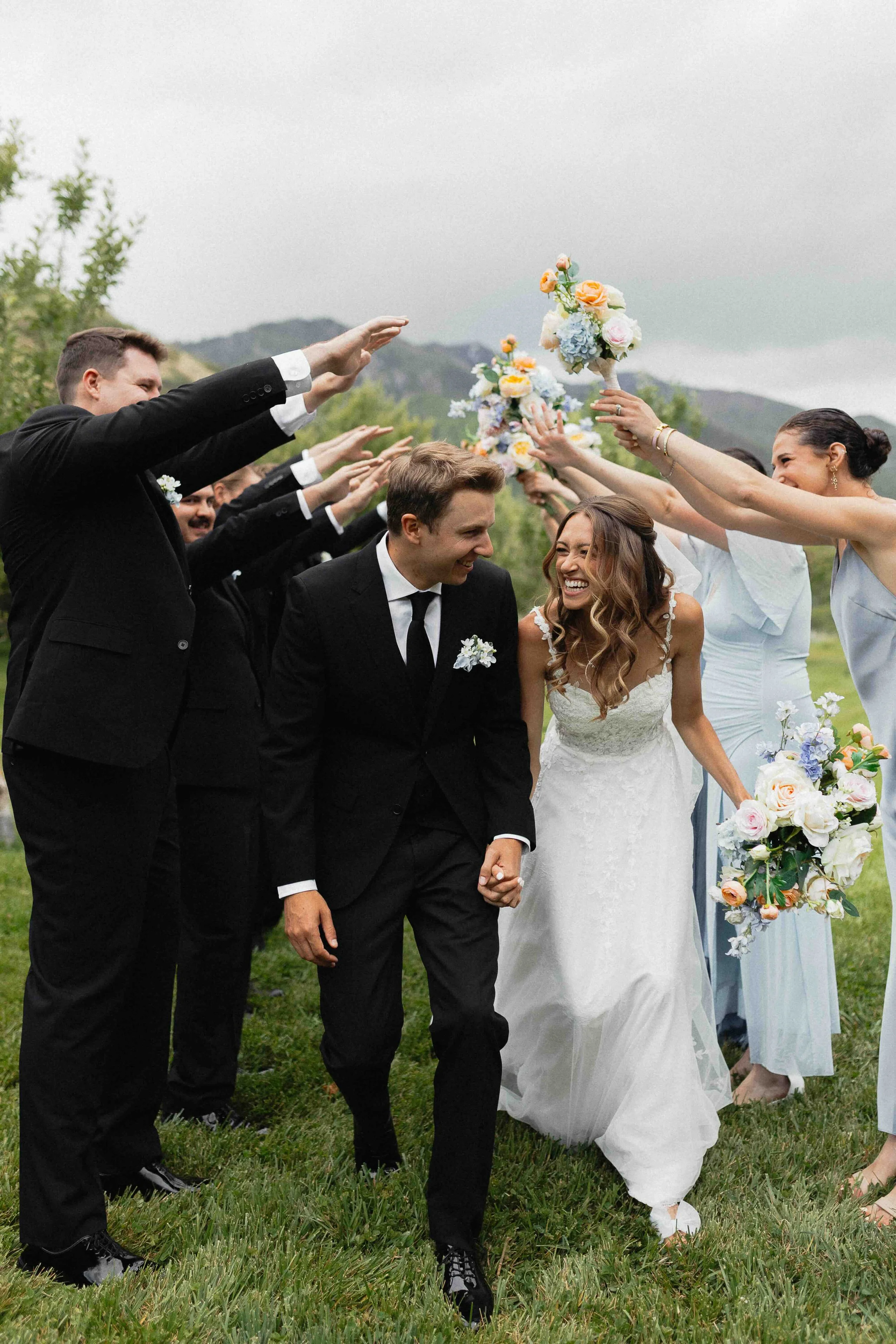 Bridesmaids and groomsmen making a tunnel with their arms as the bride and groom walk through it while laughing,