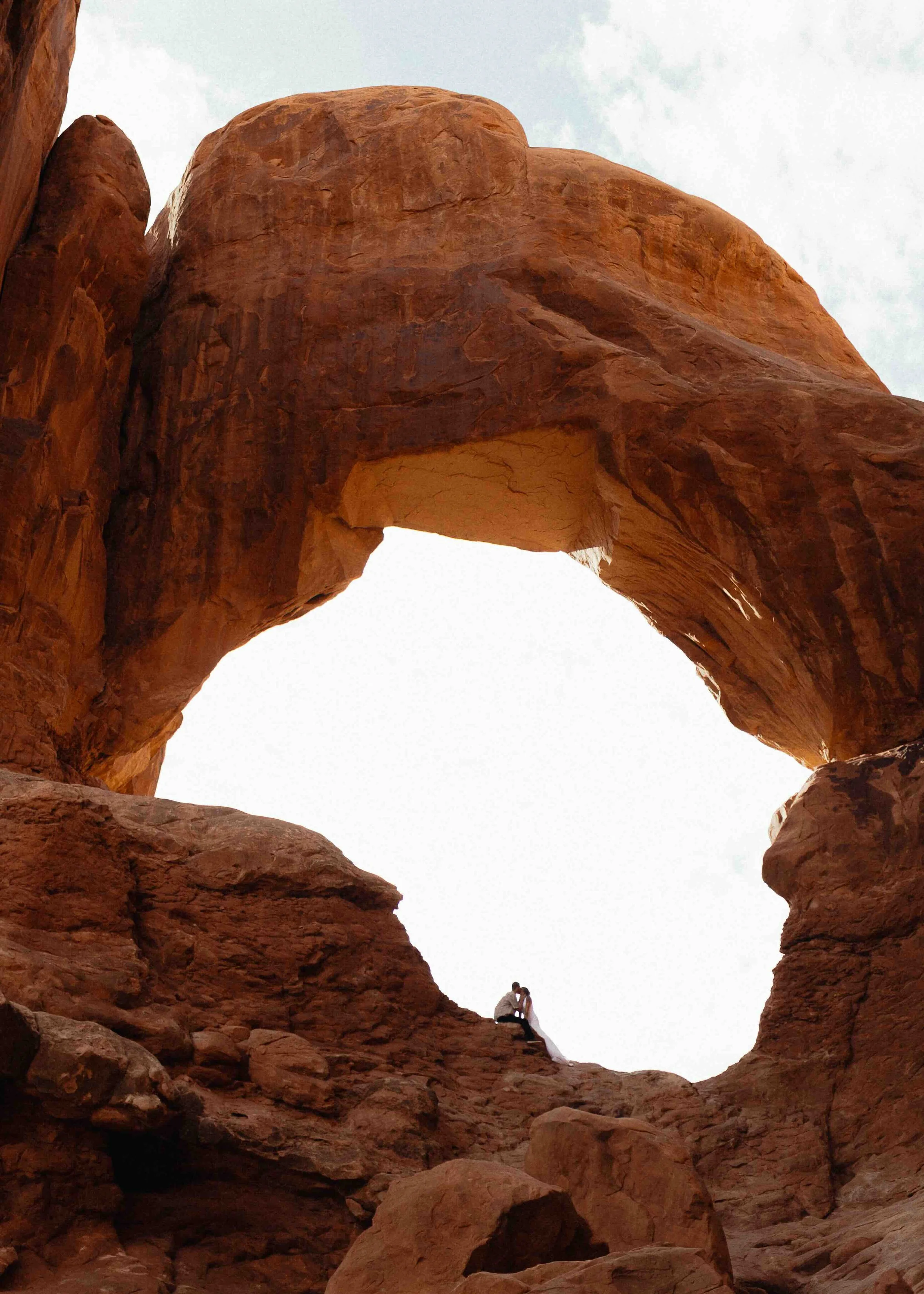 Bride and groom kissing inside of red rock  arch.