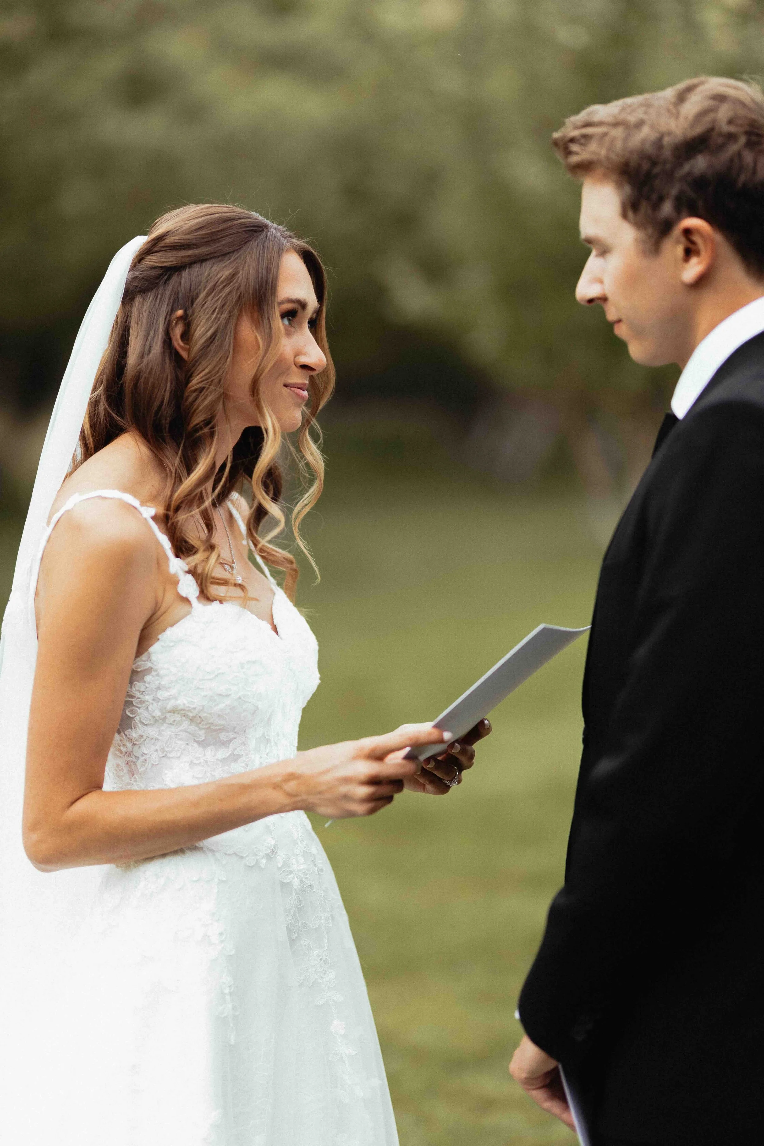 Bride reading her vows to her groom with an orchard in the background.