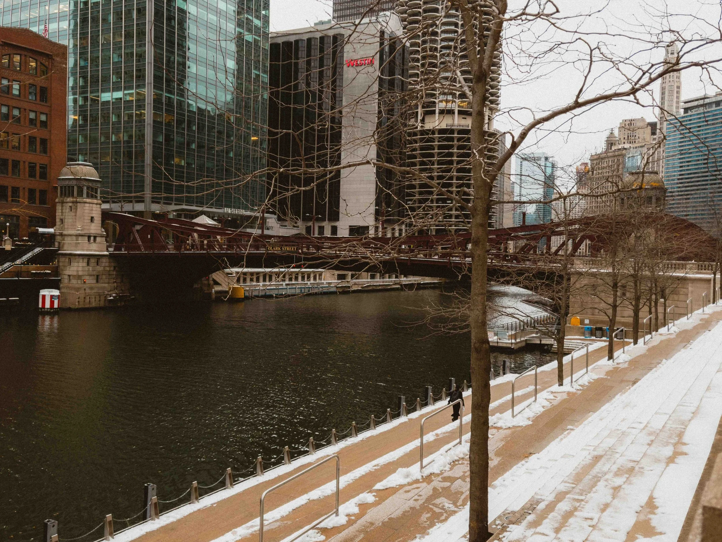 A walkway near the river with tall Chicago fountains in the background.