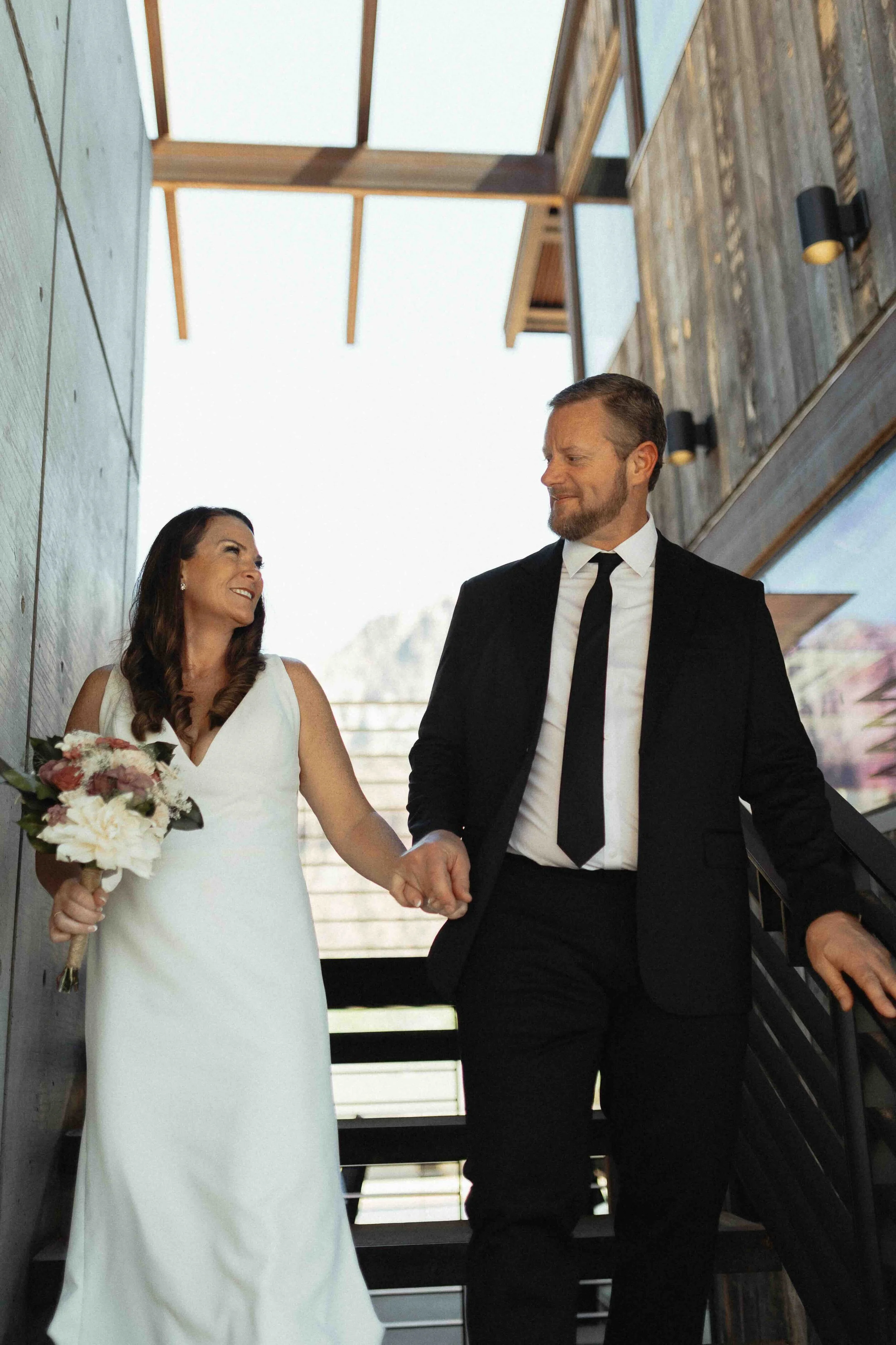 Bride and groom walking down the steps of their airbnb with concrete and wood in the background.