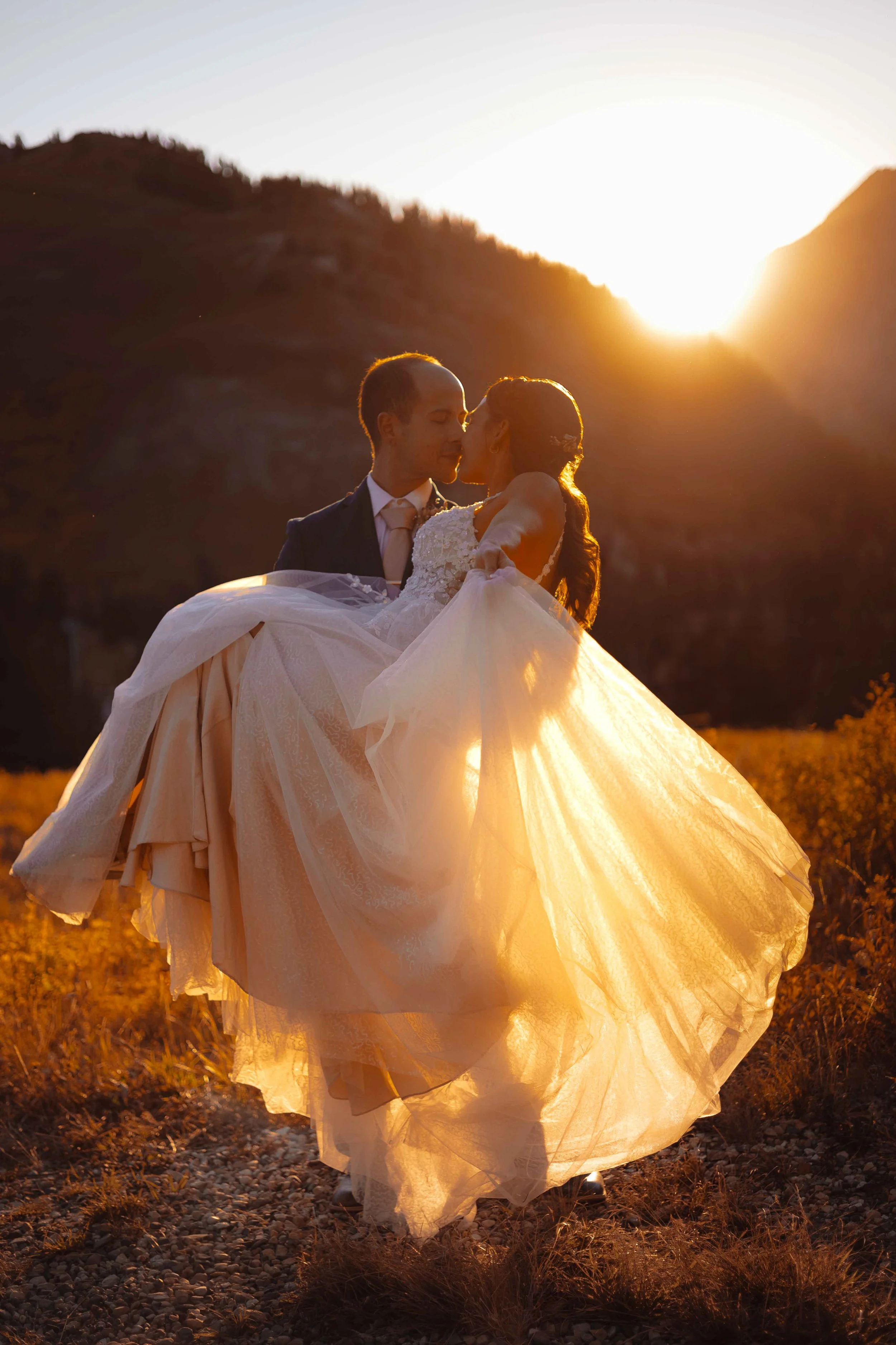 A bridal couple embracing in the sunset on a mountaintop about to kiss.