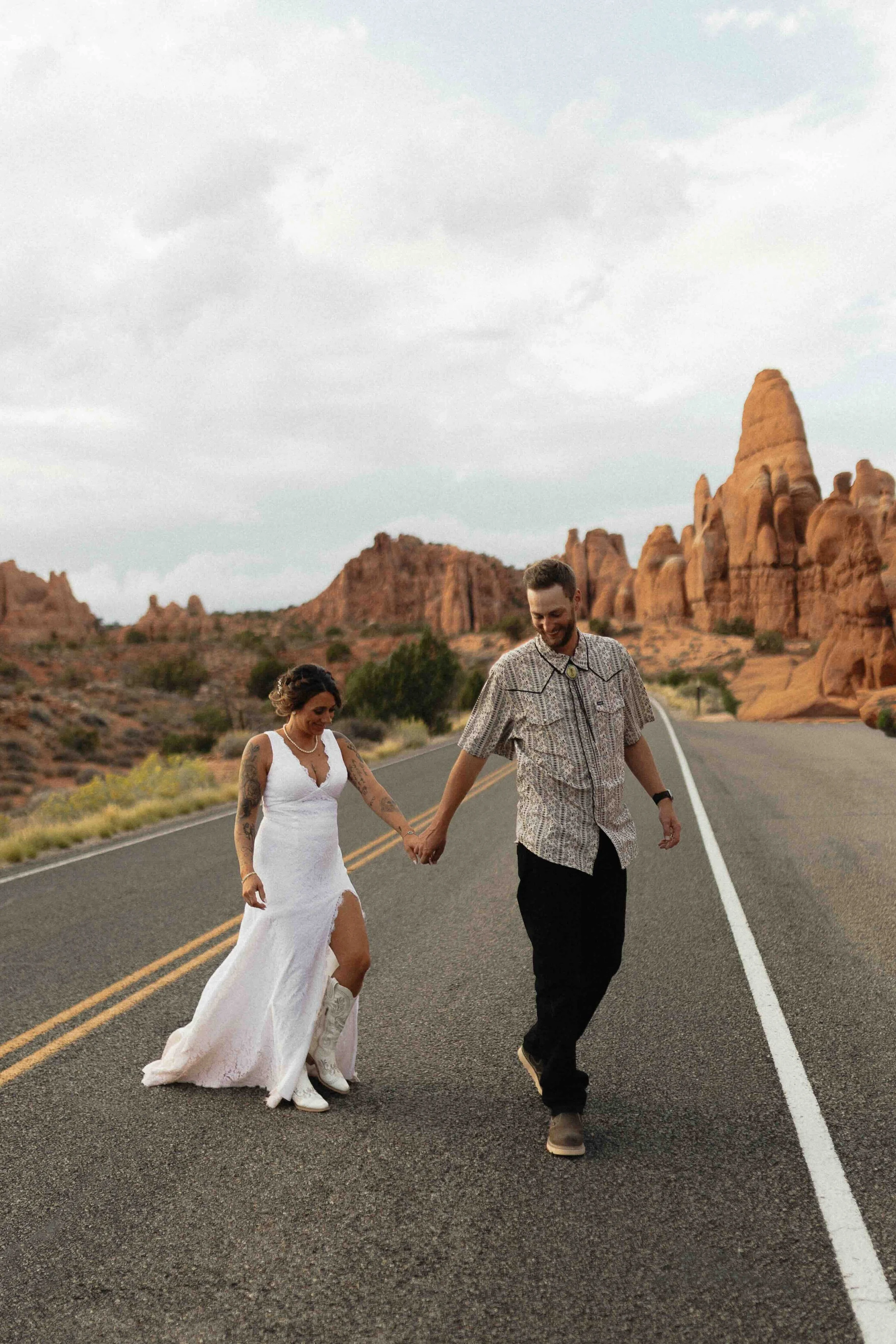 Bride and groom walking across the street in front of red rock formations in Utah.
