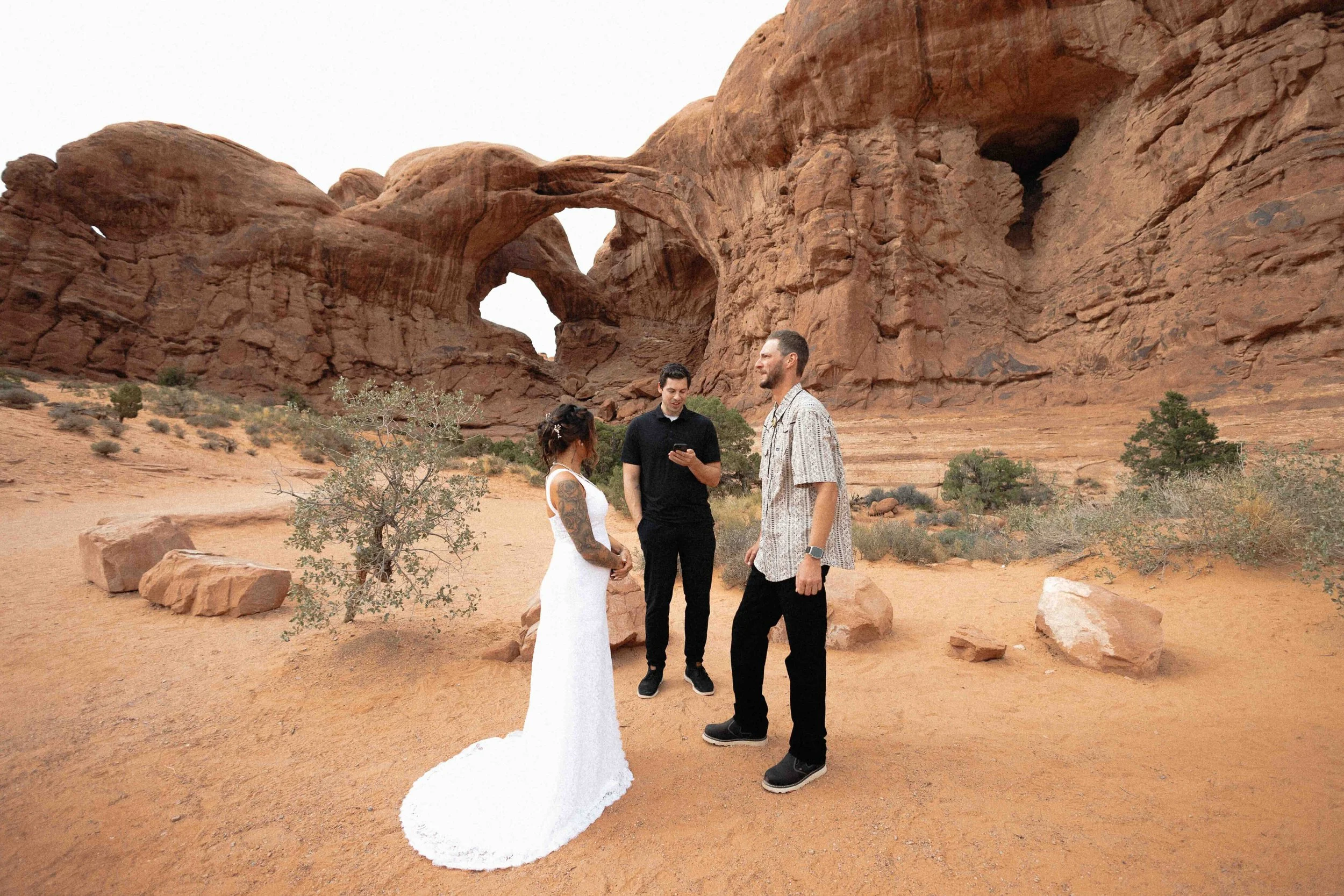 Bride and groom getting married by an officiant in all black. They are standing in front of the double arch in Moab.