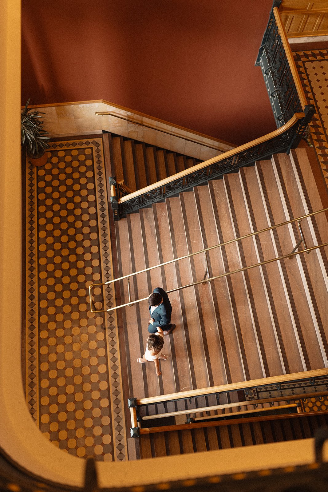 Bride and groom walking down a vintage staircase with gold tones and embellishments.