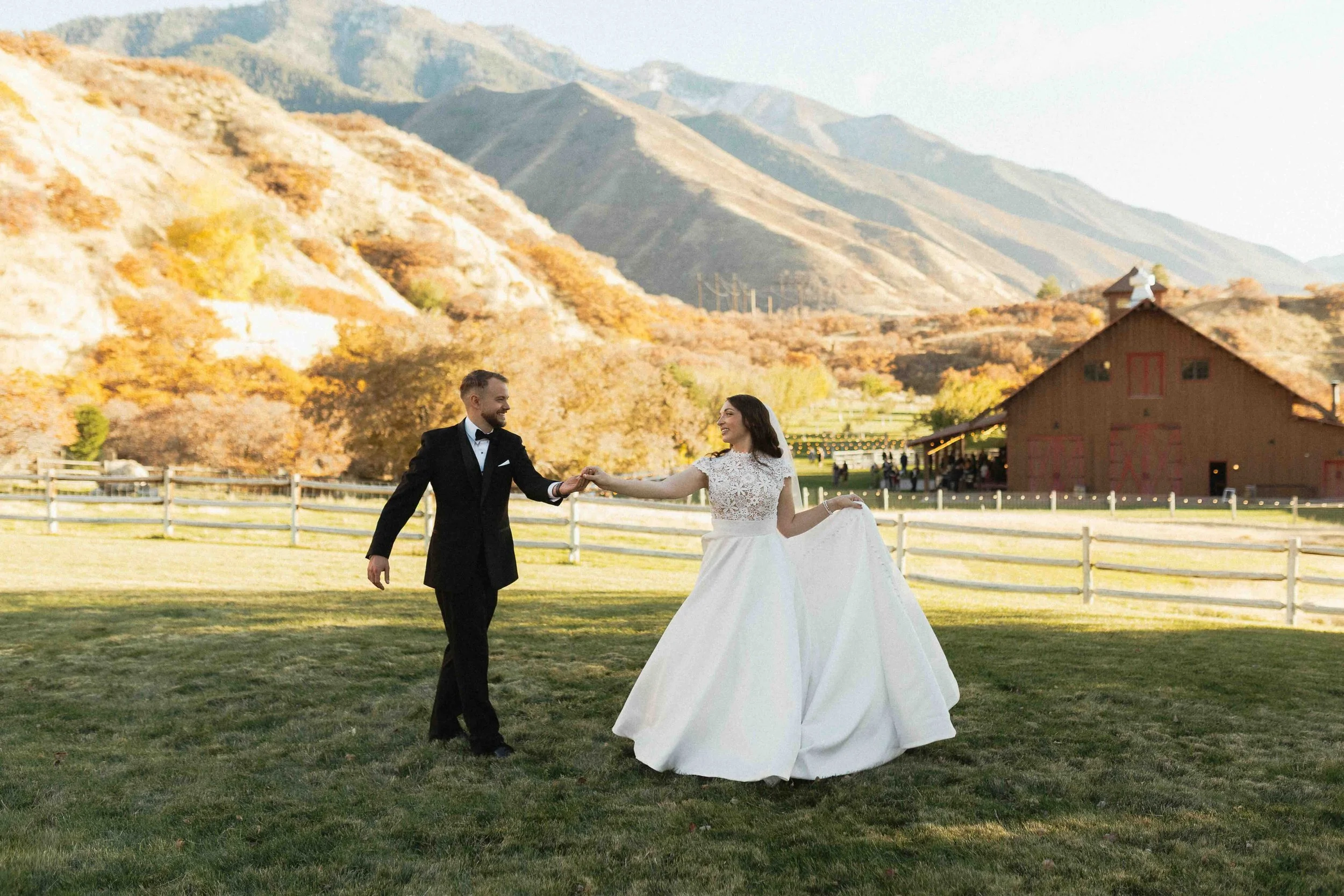 Groom escorting bride through a field in front of mountain view with a barn in the background.