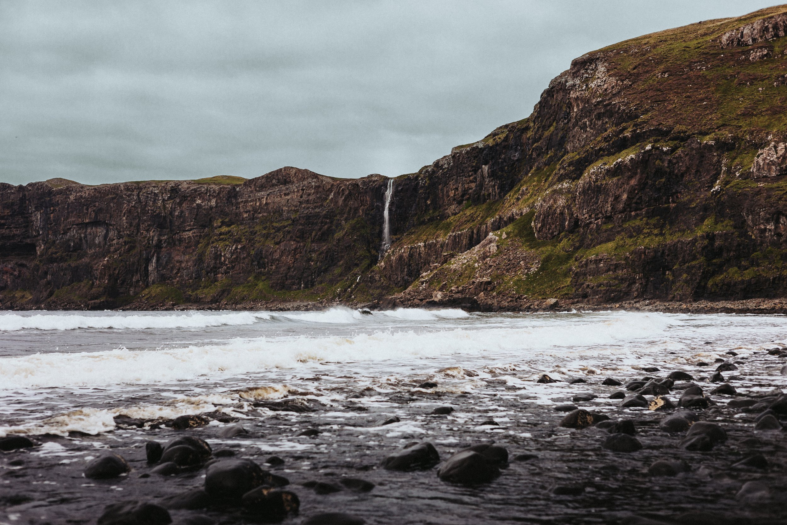 Black rock beach with waterfall going over cliffside in the distance
