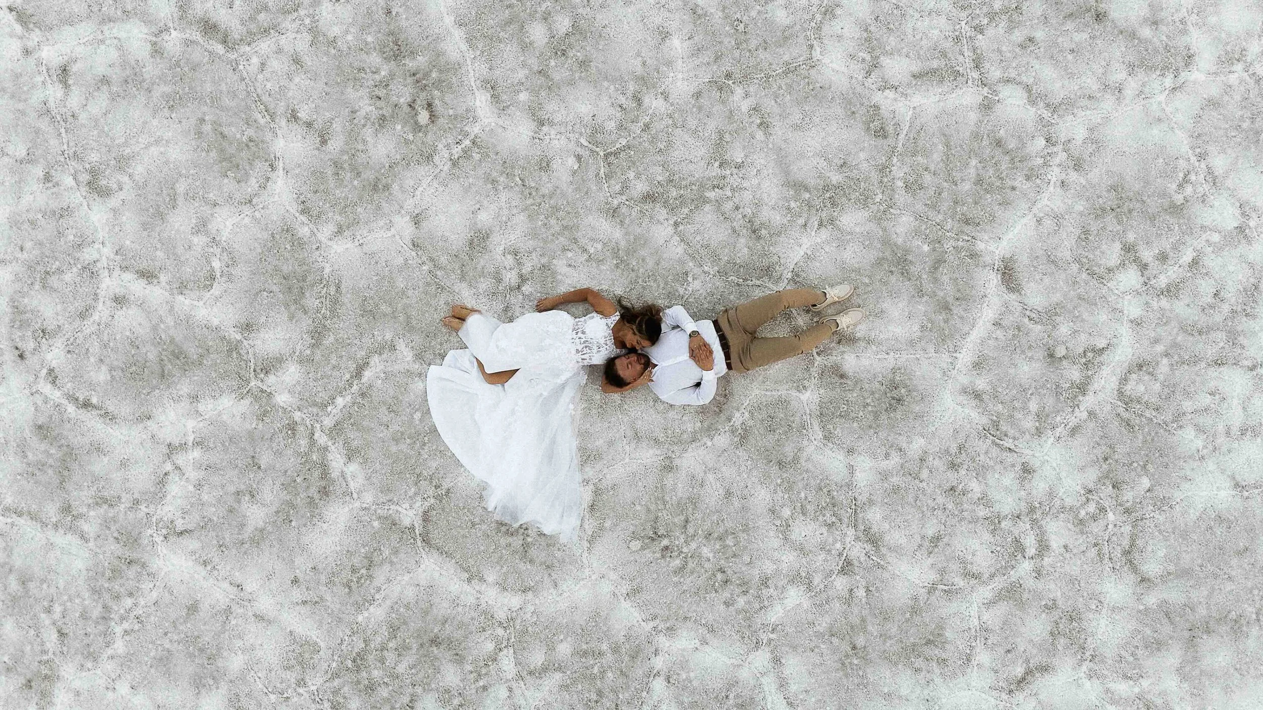 Bride and groom laying on the Salt Flats of Wendover Utah. It is an aerial shot from a drone.