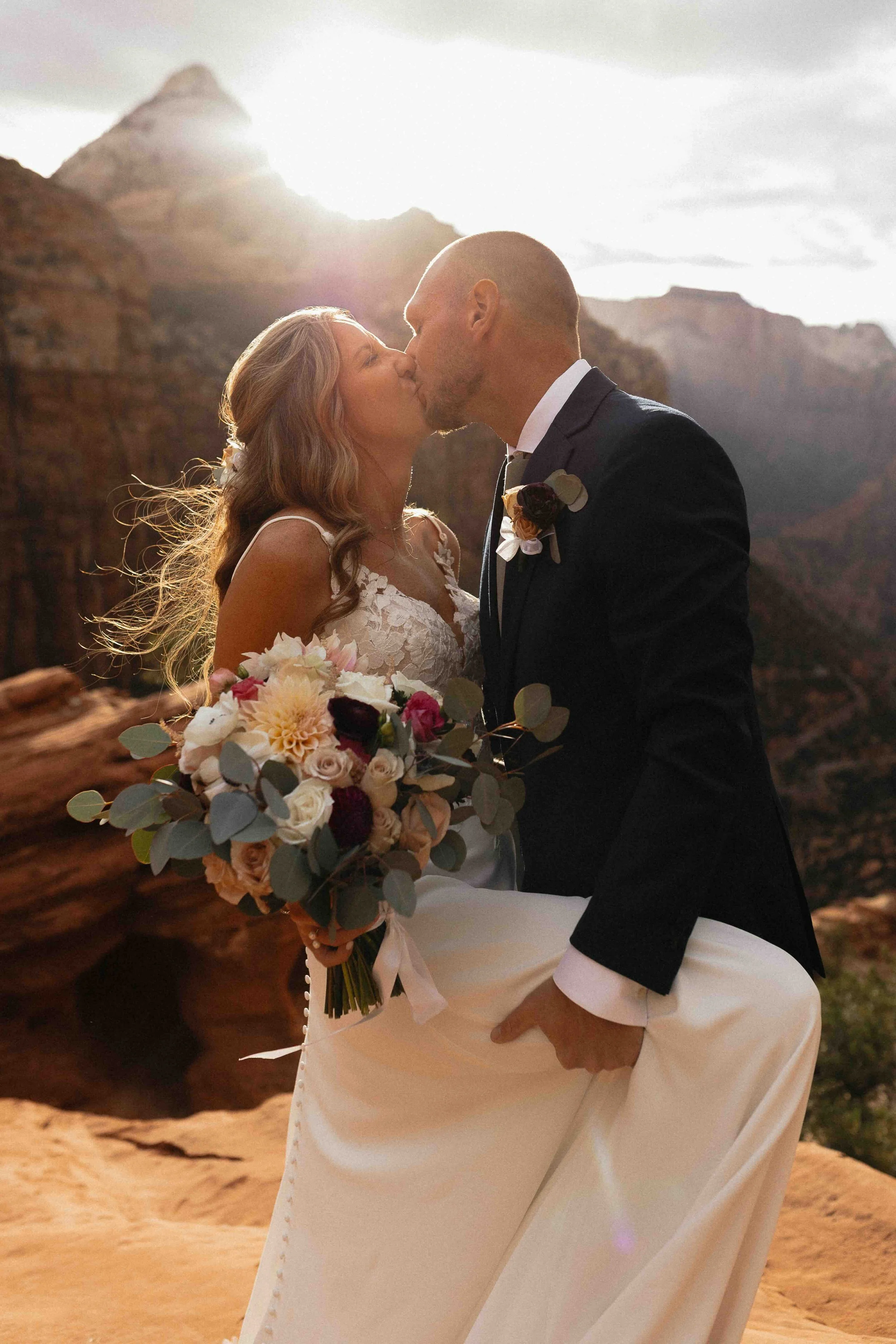 Bride and groom kissing in front of Zion National Park rocks in the background as the sun is setting.