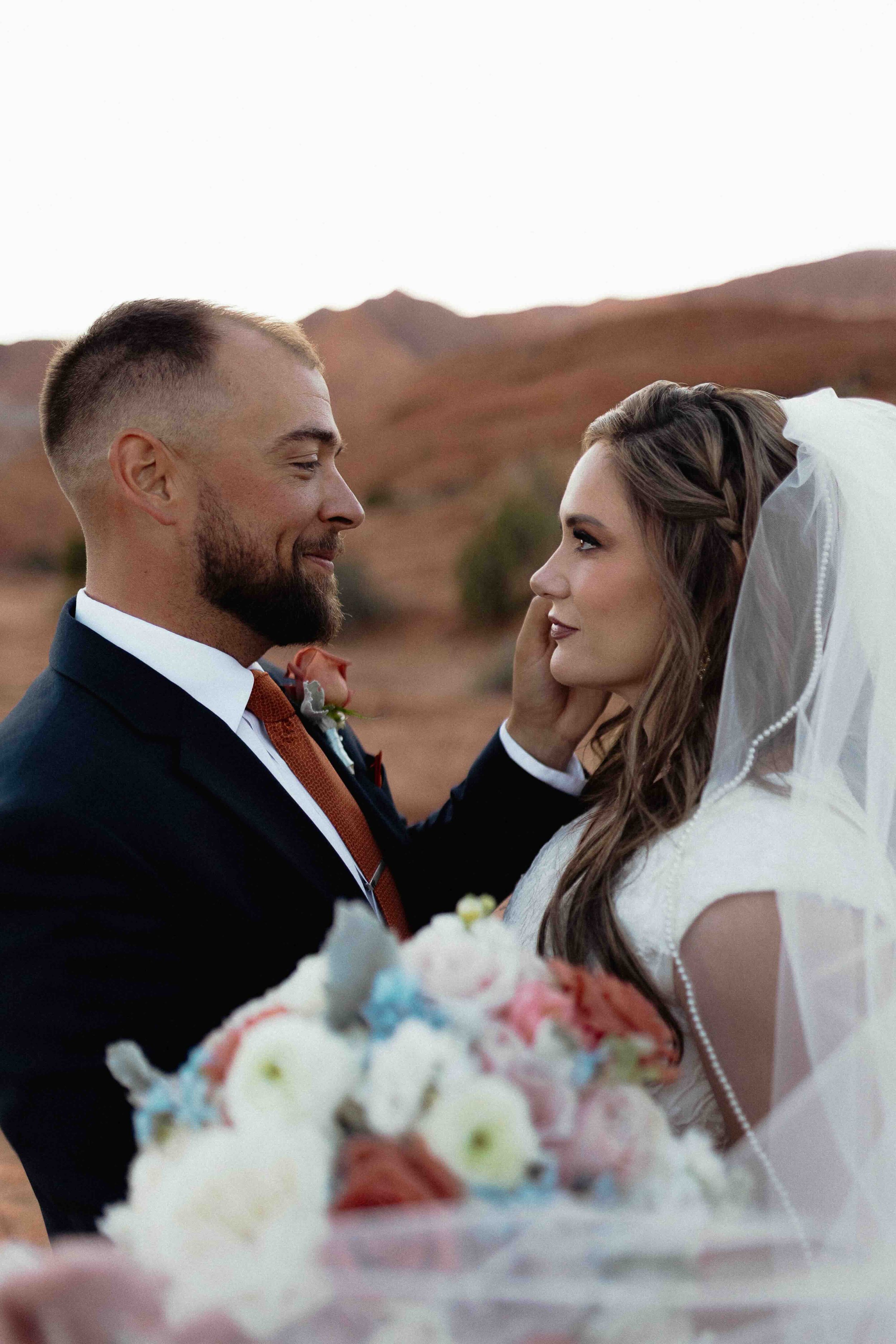 Groom touching bride's cheek at Snow Canyon State Park in St. George UT with red rock in the background.