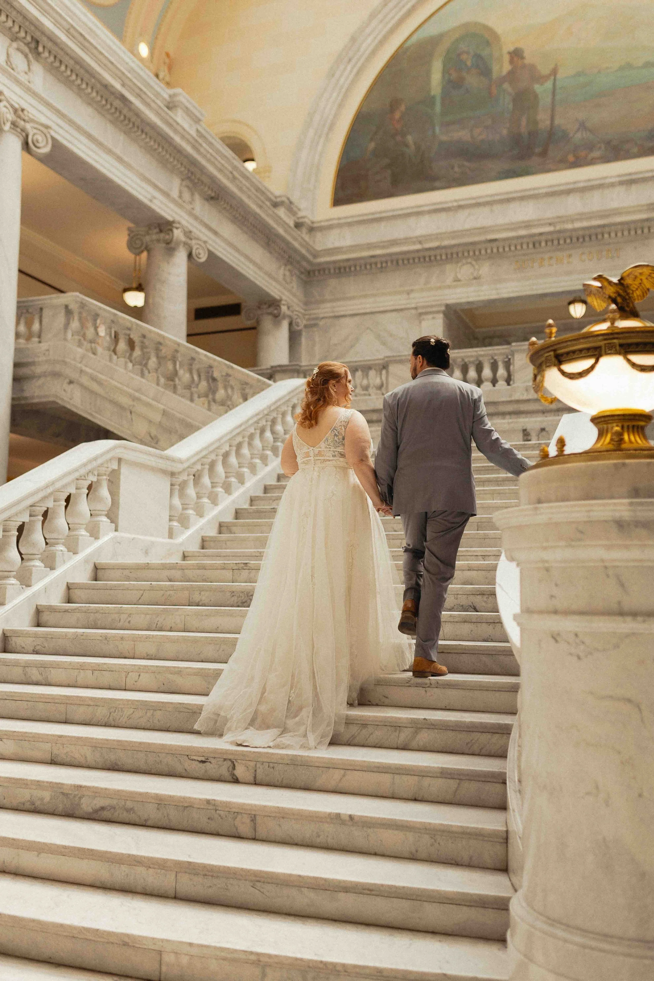 Bride and groom walking up marbled stairs in a capitol building.