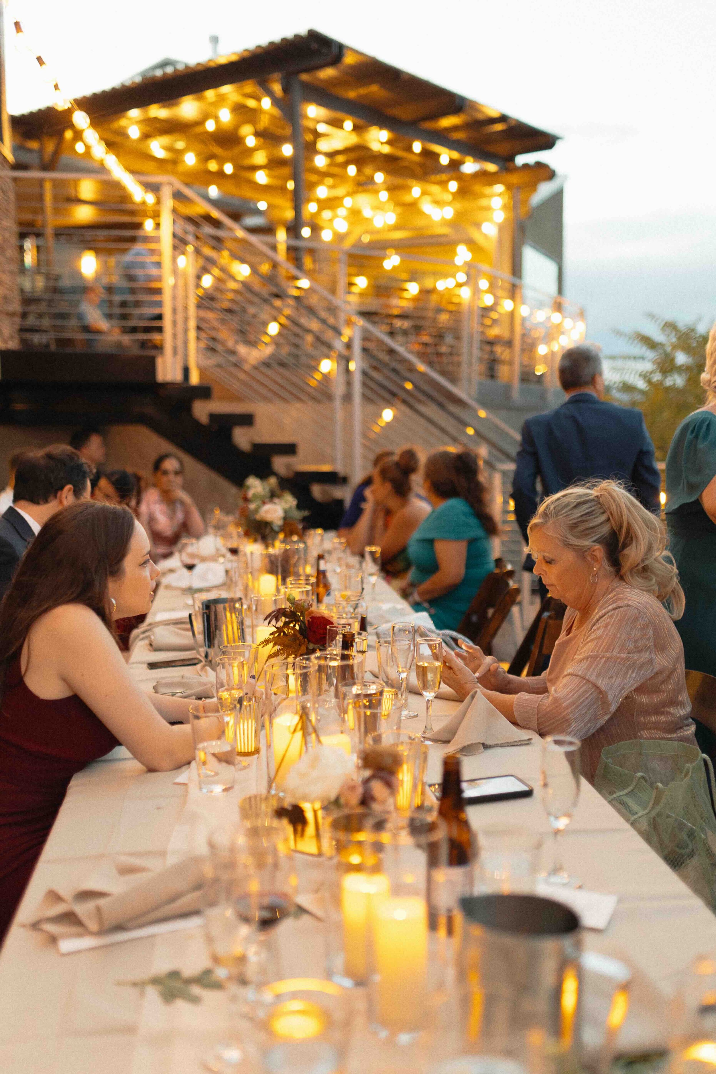 a reception with guests sitting at a lit table with twinkling lights in the background.