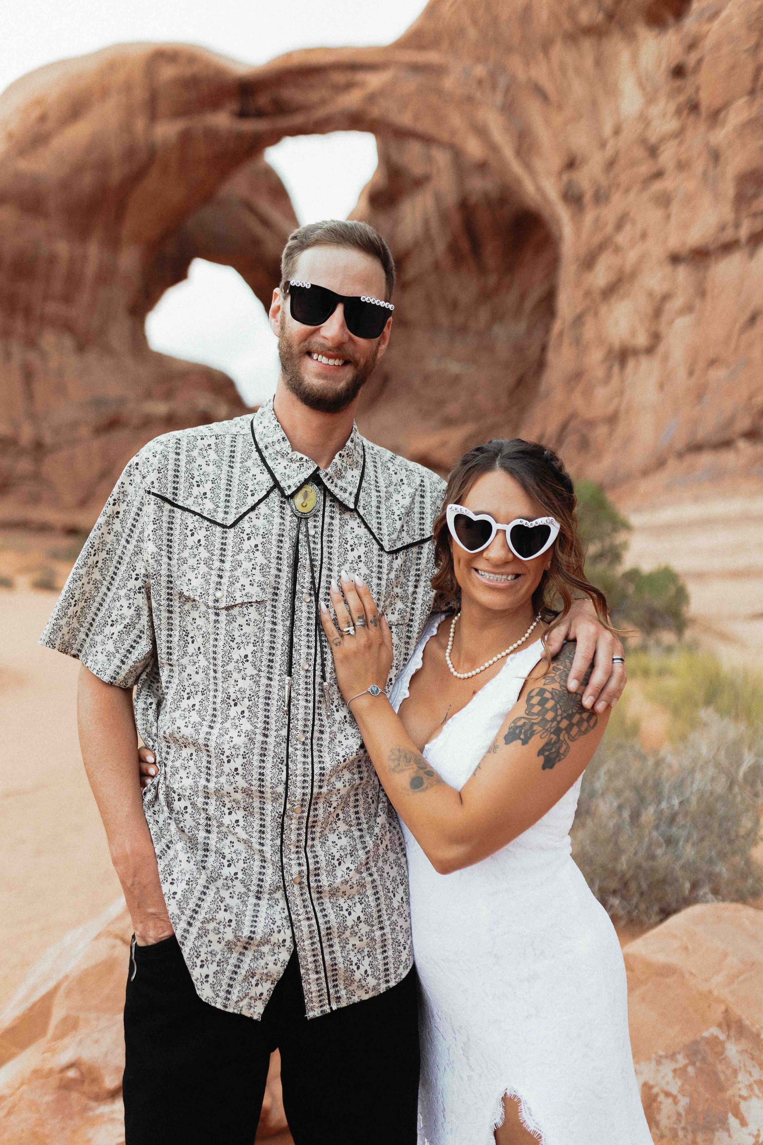 Bride and room standing in front of the double arch in Moab with sunglasses on.