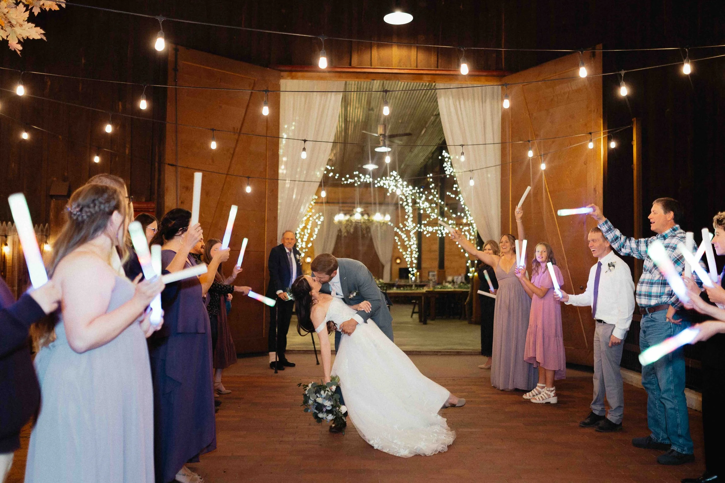Bride and groom dipping and kissing with their cheering family and friends holding onto light wands around them.