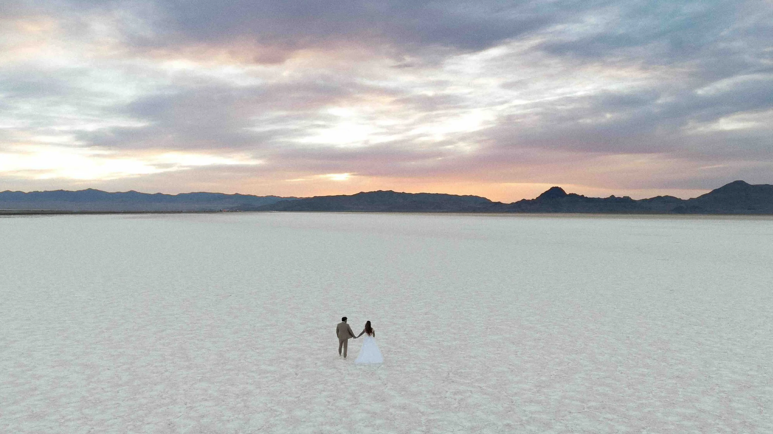 Aerial drone shot of the salt flats of utah and a bride and groom are holding hands from a distance.