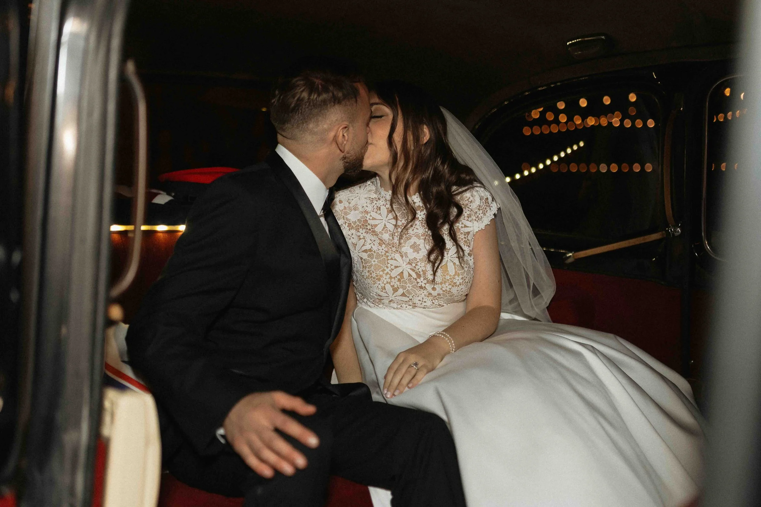 Bride and groom kissing inside of their black London Limo getaway car.