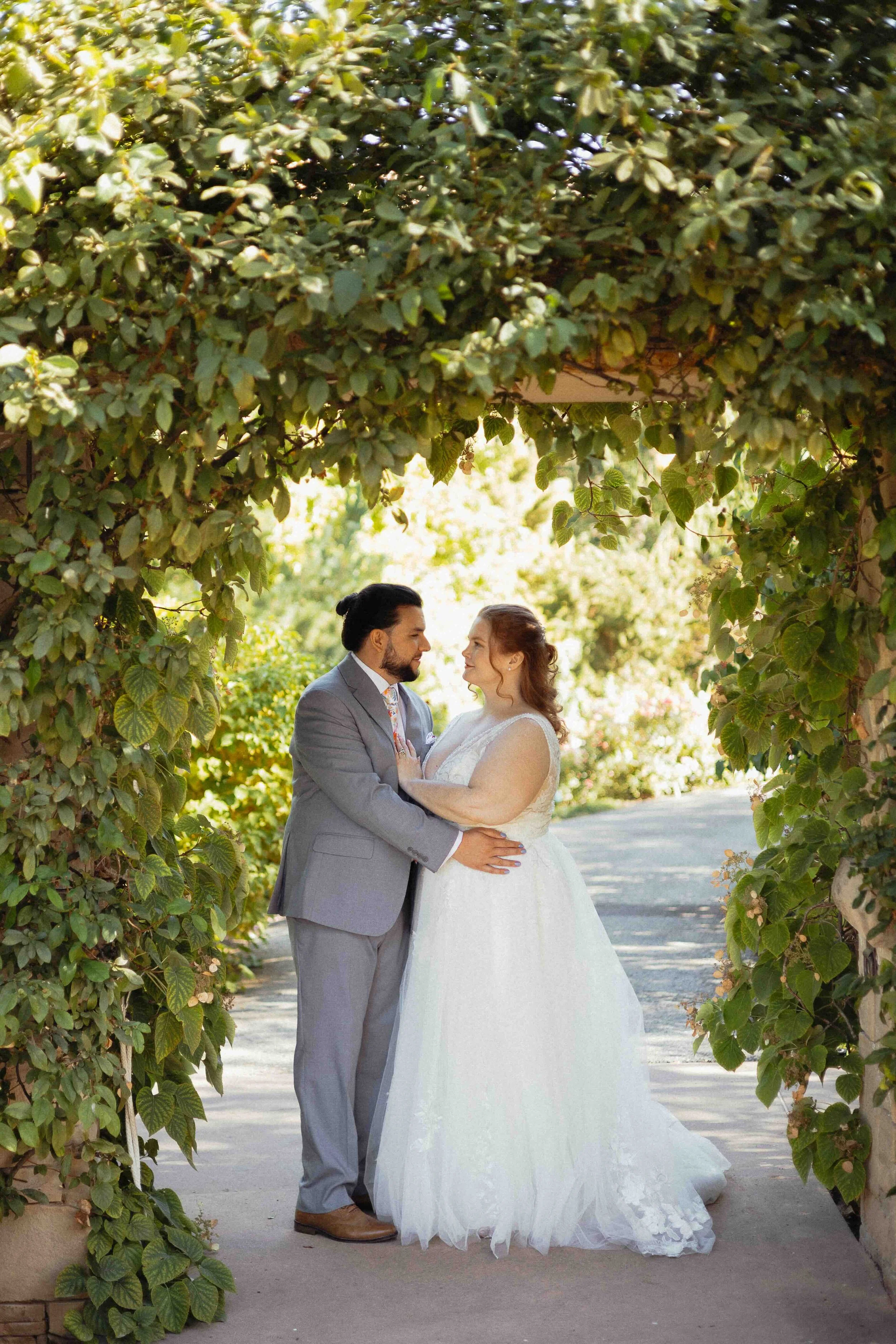 Bridal couple looking into each other's eyes under an arch covered in ivy.