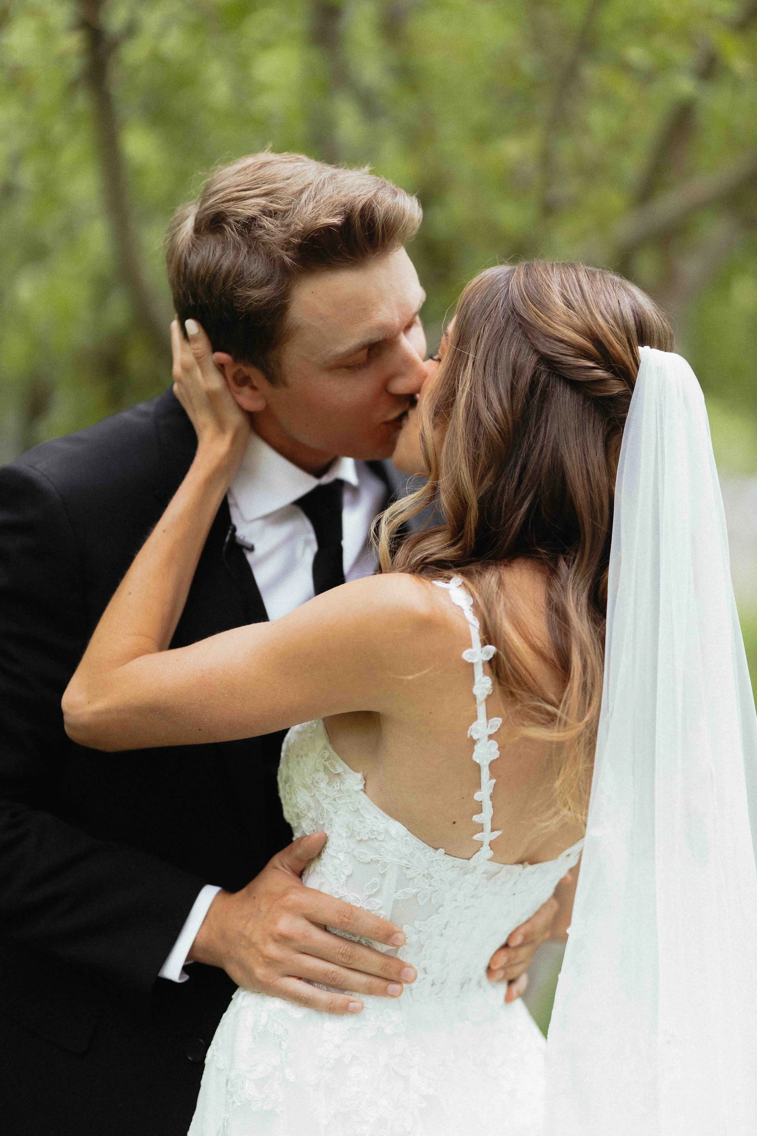 Bride and groom kissing in front of a green tree.