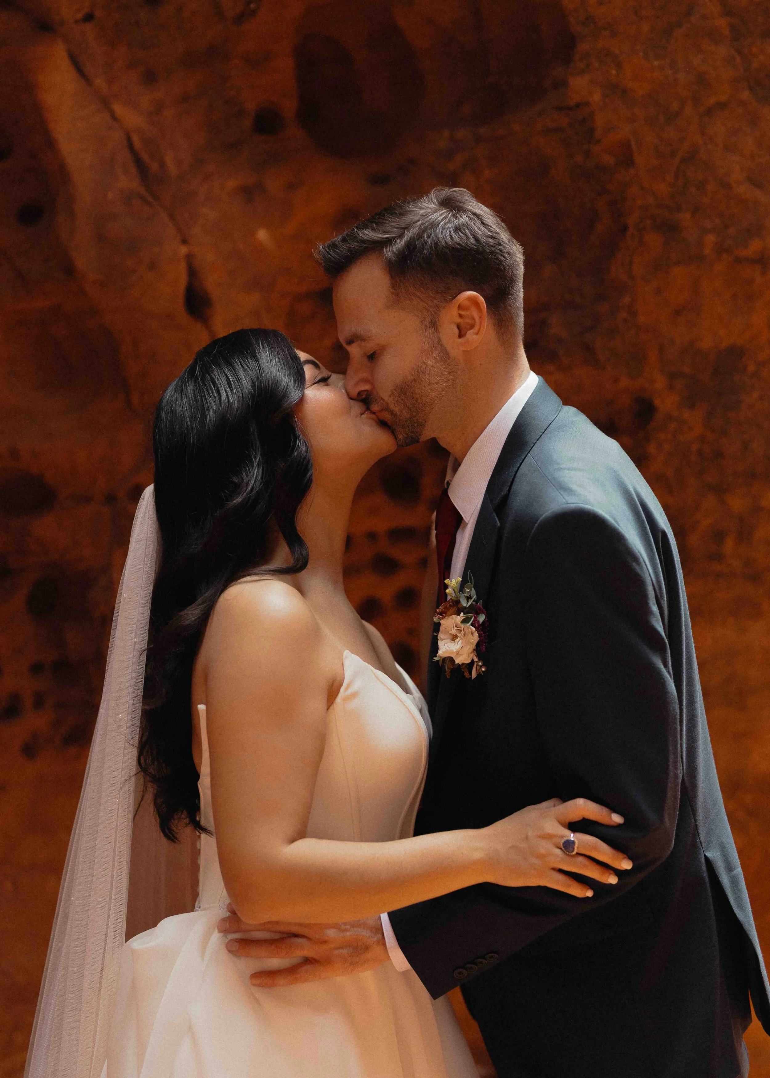 a bride and groom kissing in front of red rock.