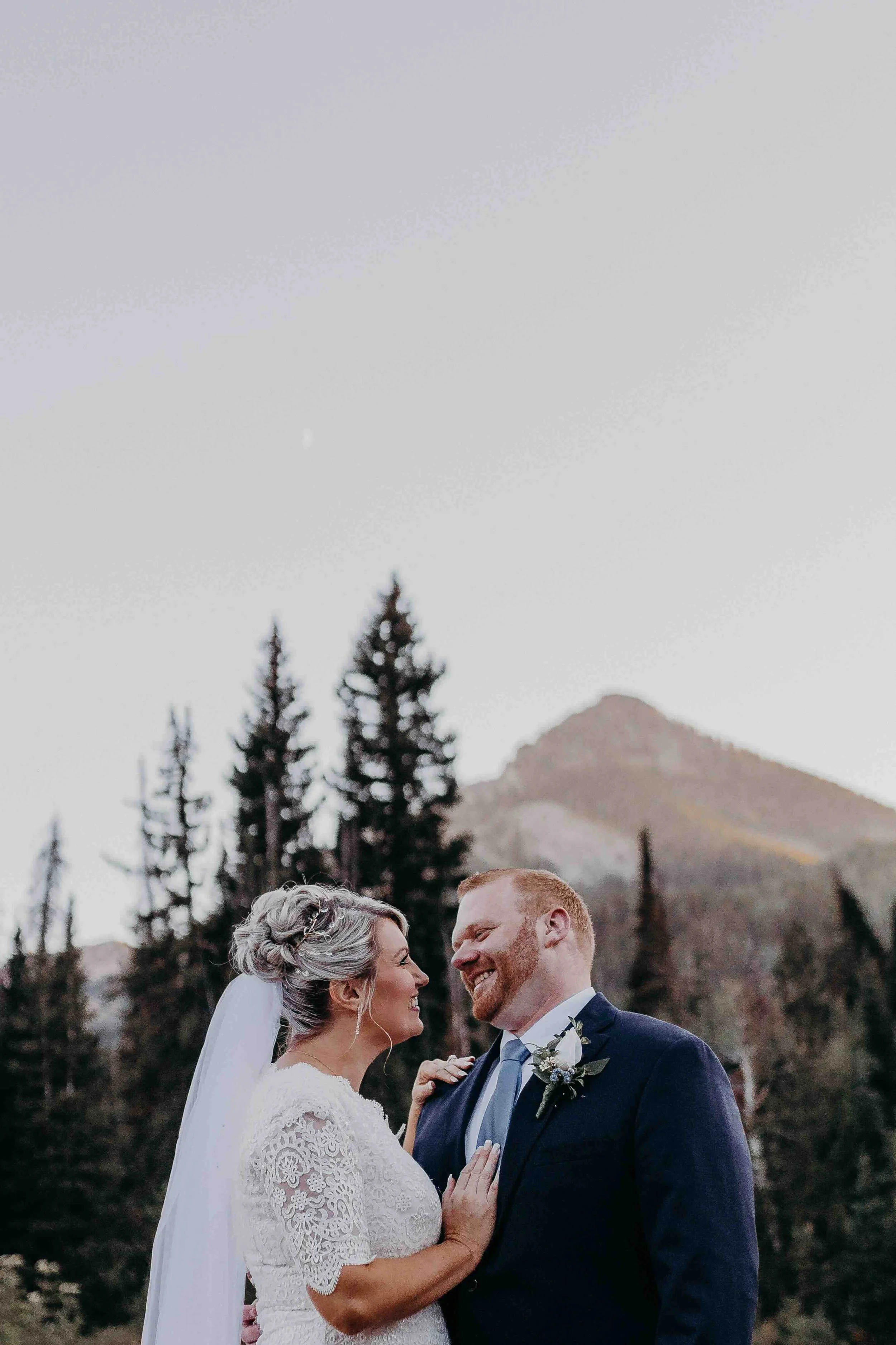 Bride and groom looking at each other in front of a mountain peak and pine trees.
