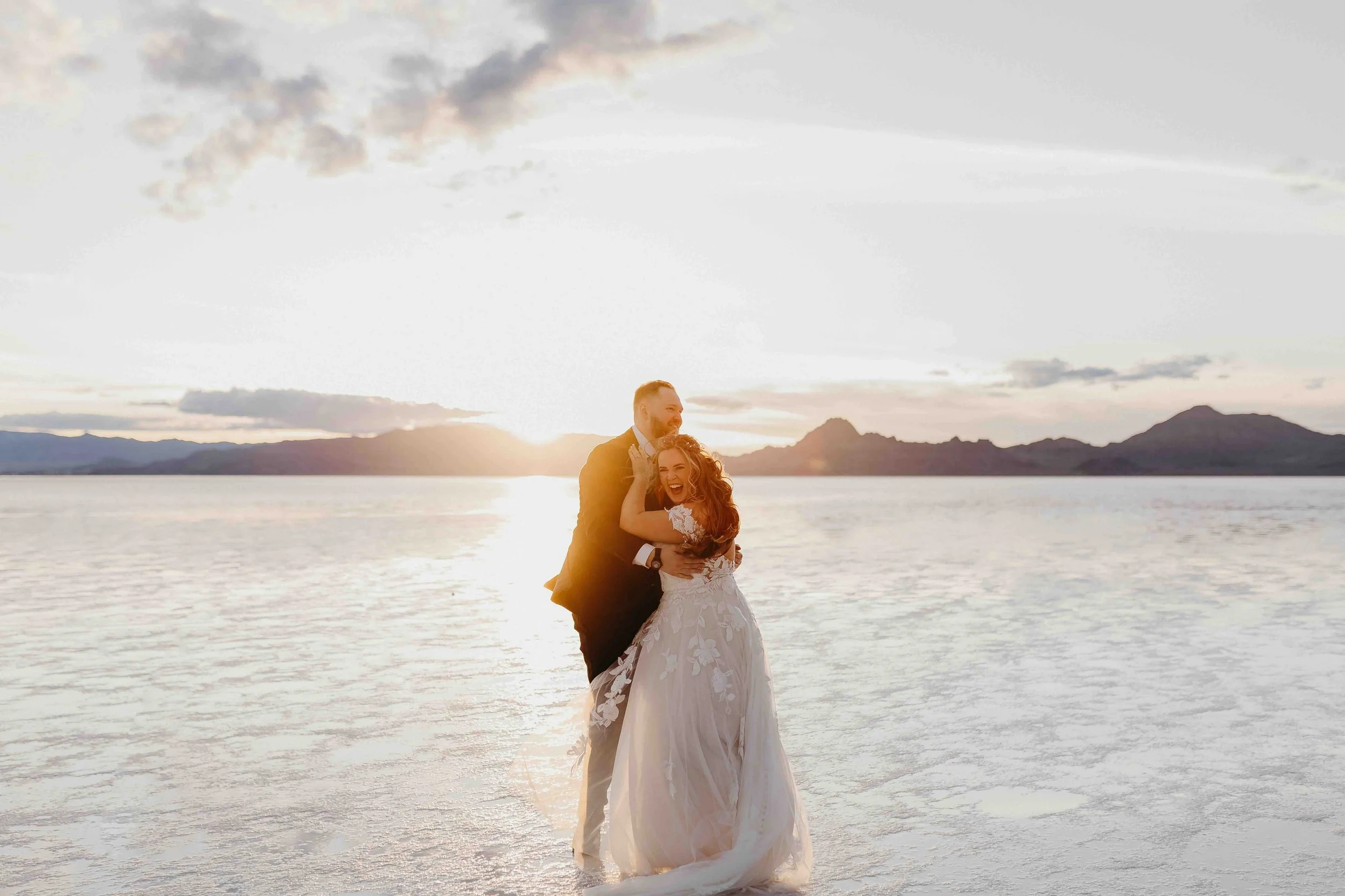 Bride and groom laughing together at the Bonneville Salt Flats during sunset.