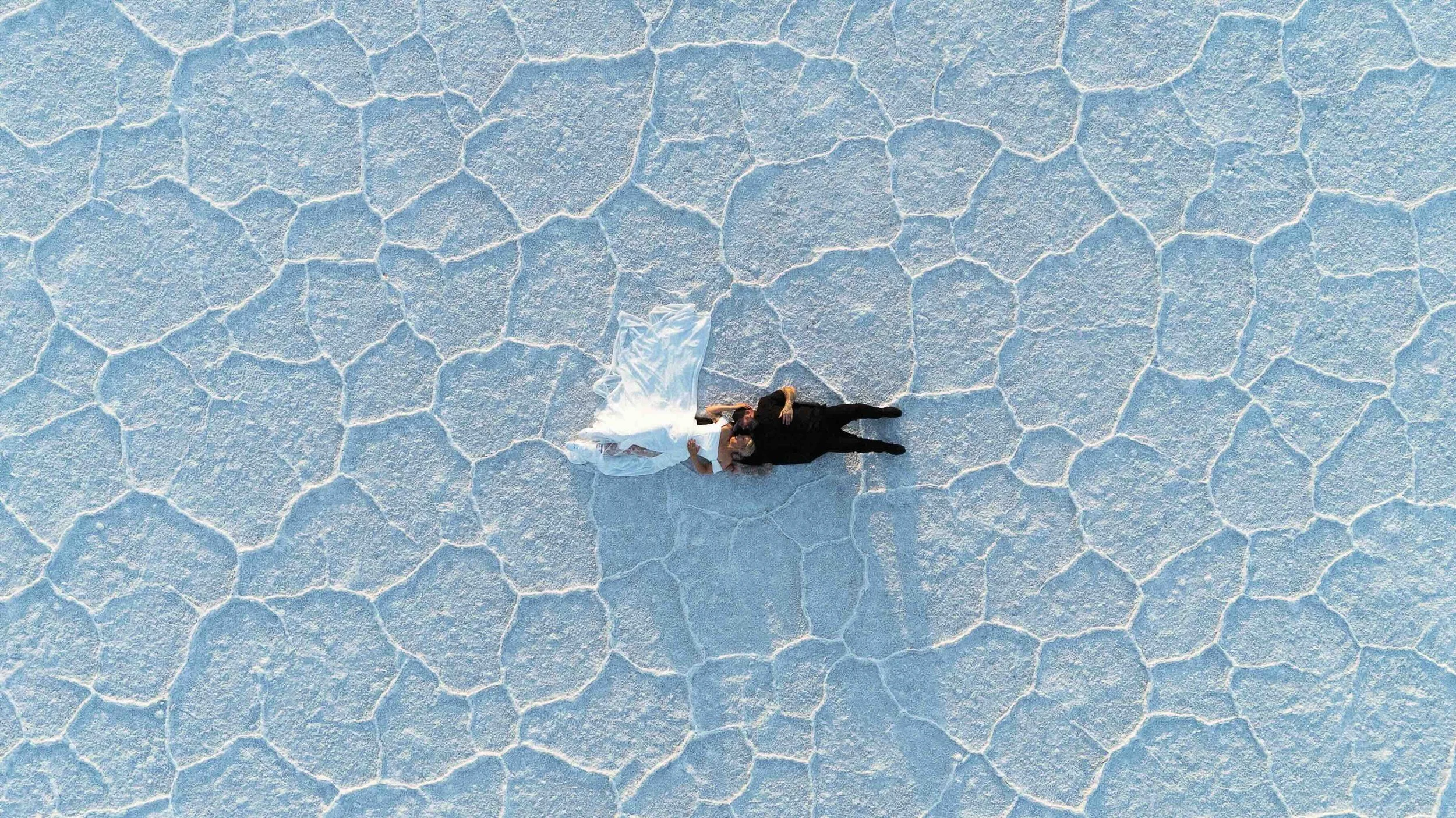 Bride and groom laying down on the Bonneville salt flats from an aerial shot.