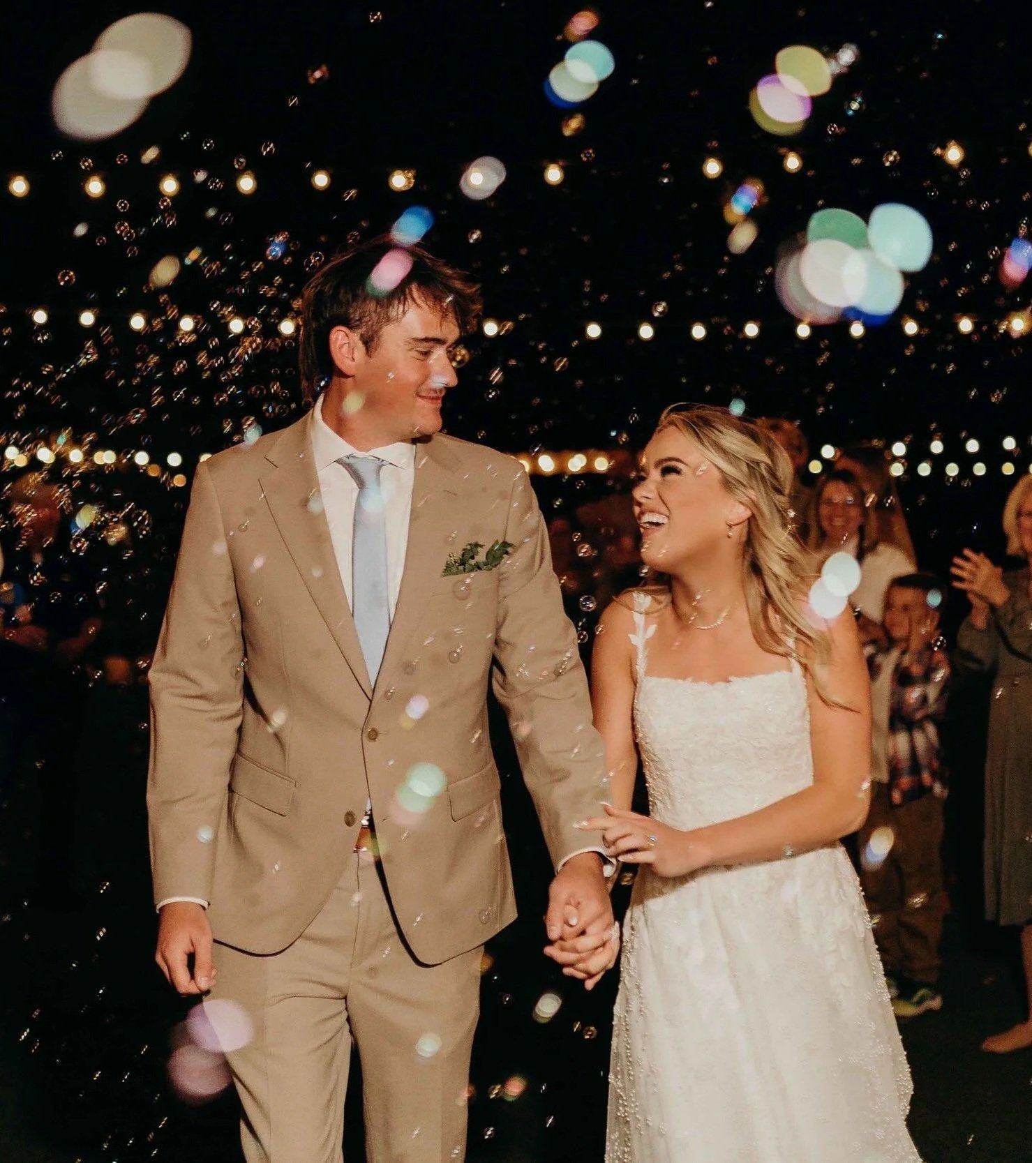 Bride and groom walking through bubbles being blown at their wedding exit at night.