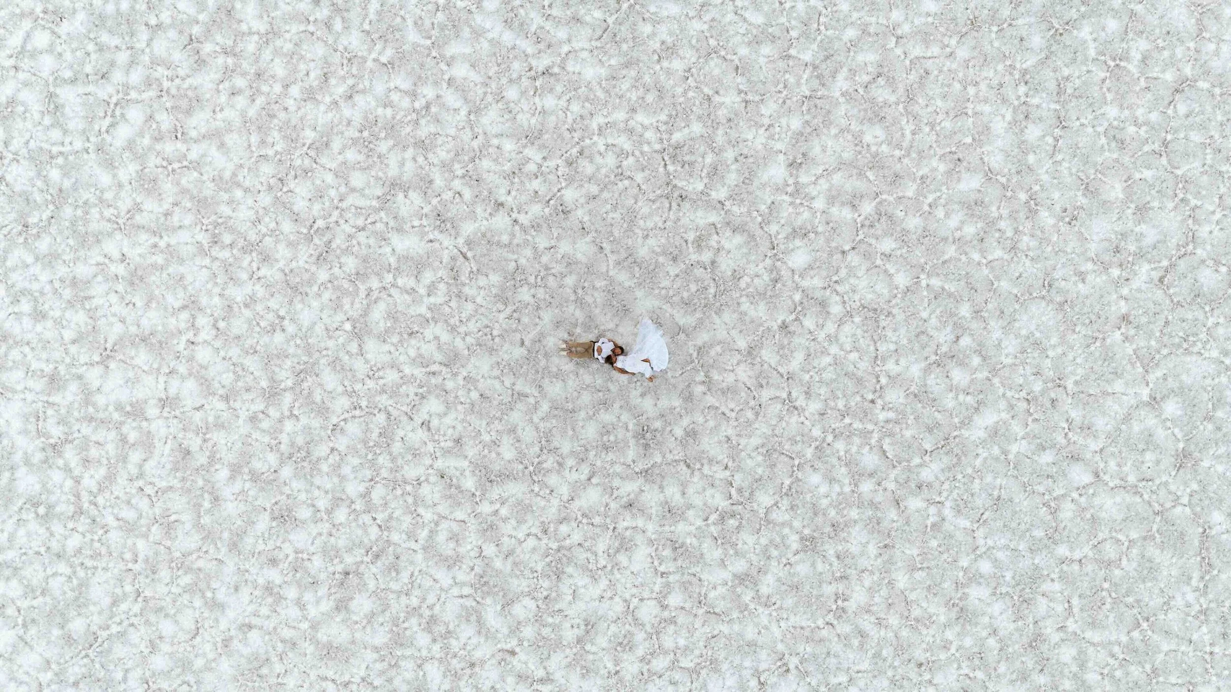 Aerial drone shot of a bride and groom laying on the salt flats of Utah.