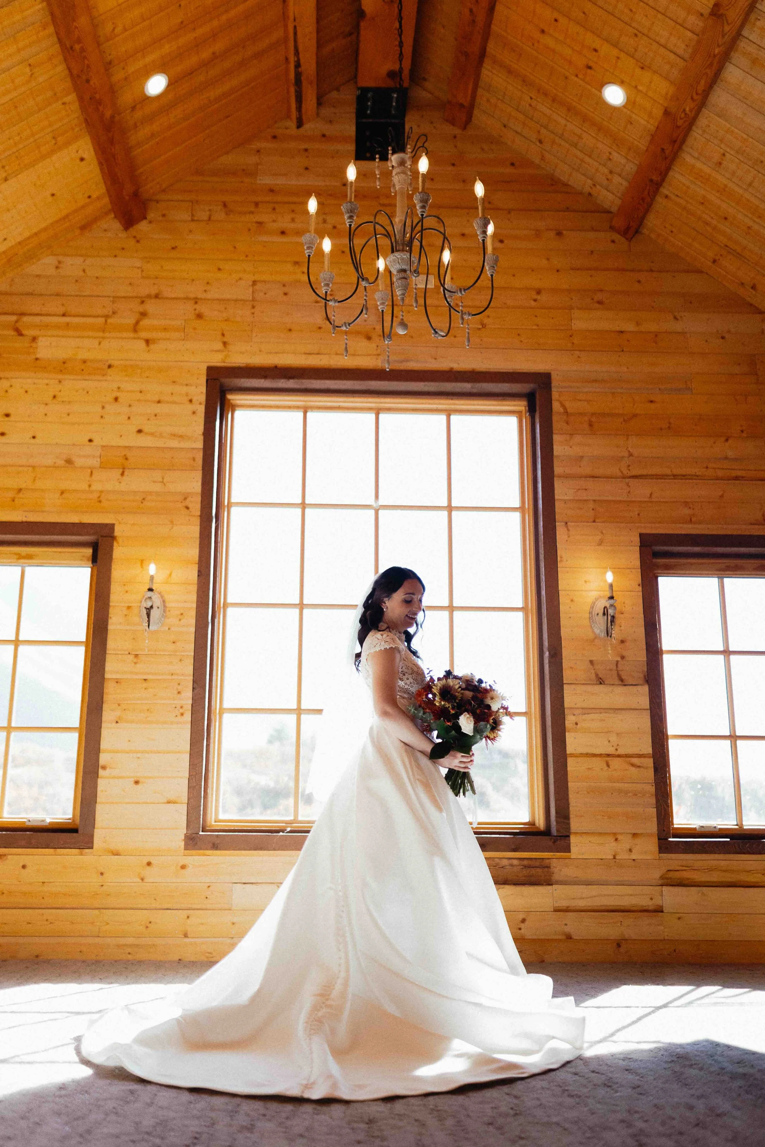 Bride holding her bouquet and standing in a bridal suite at a barn with wood and large windows letting in light.