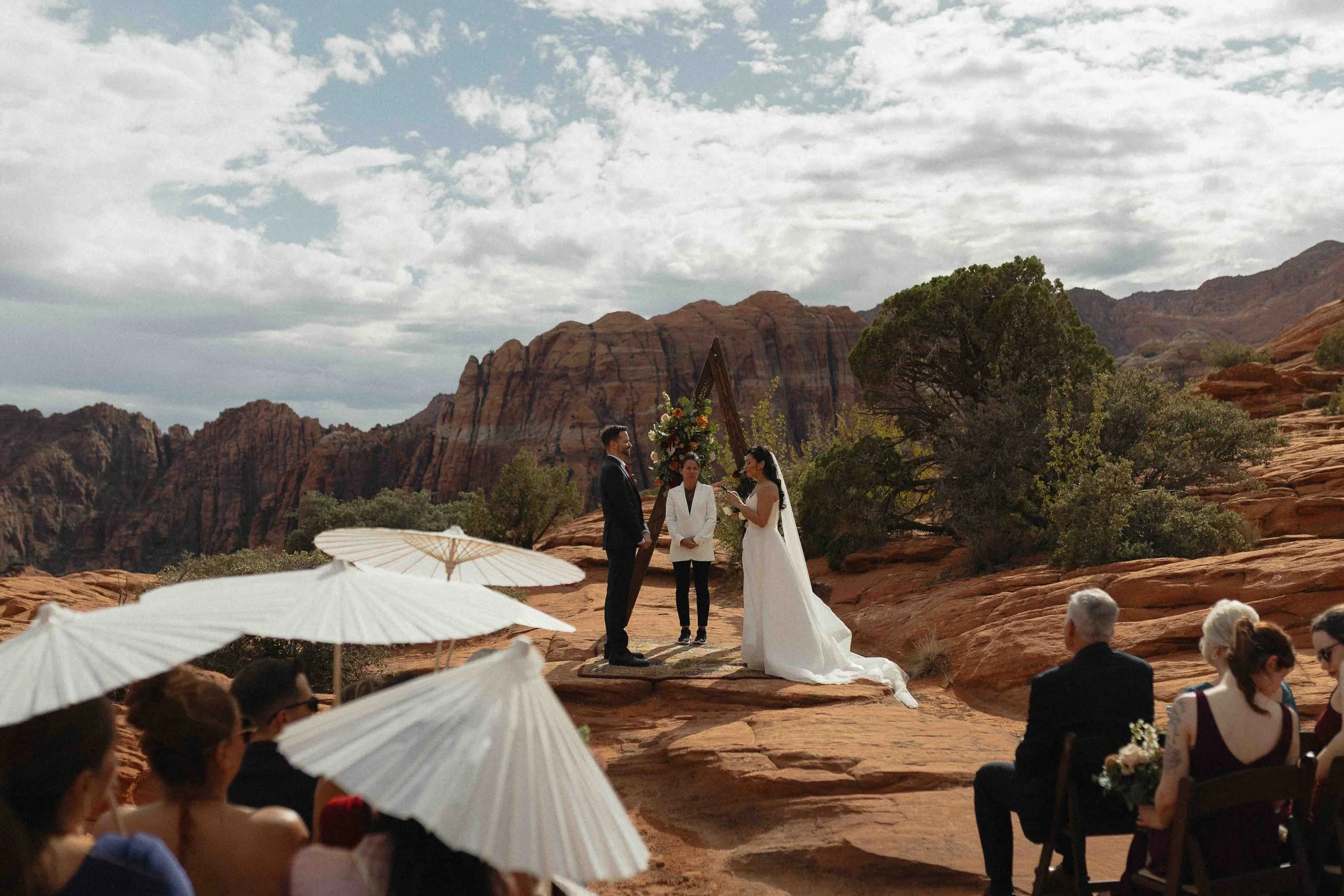 a ceremony where a bride and groom are marrying on the petrified dunes of utah. Guests are holding parasols.
