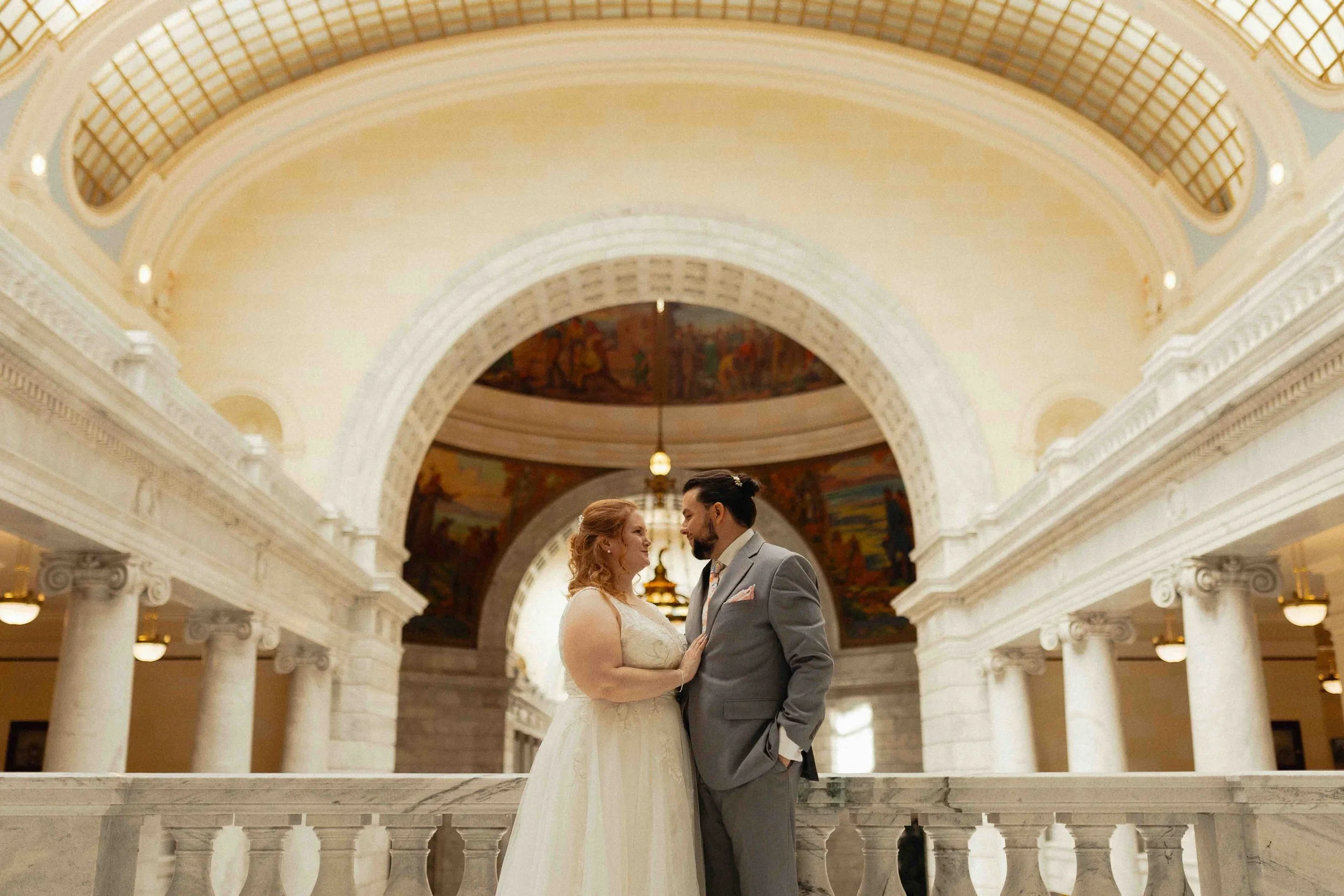 Bride and groom standing in a capitol building with columns in the background and a curved ceiling,.