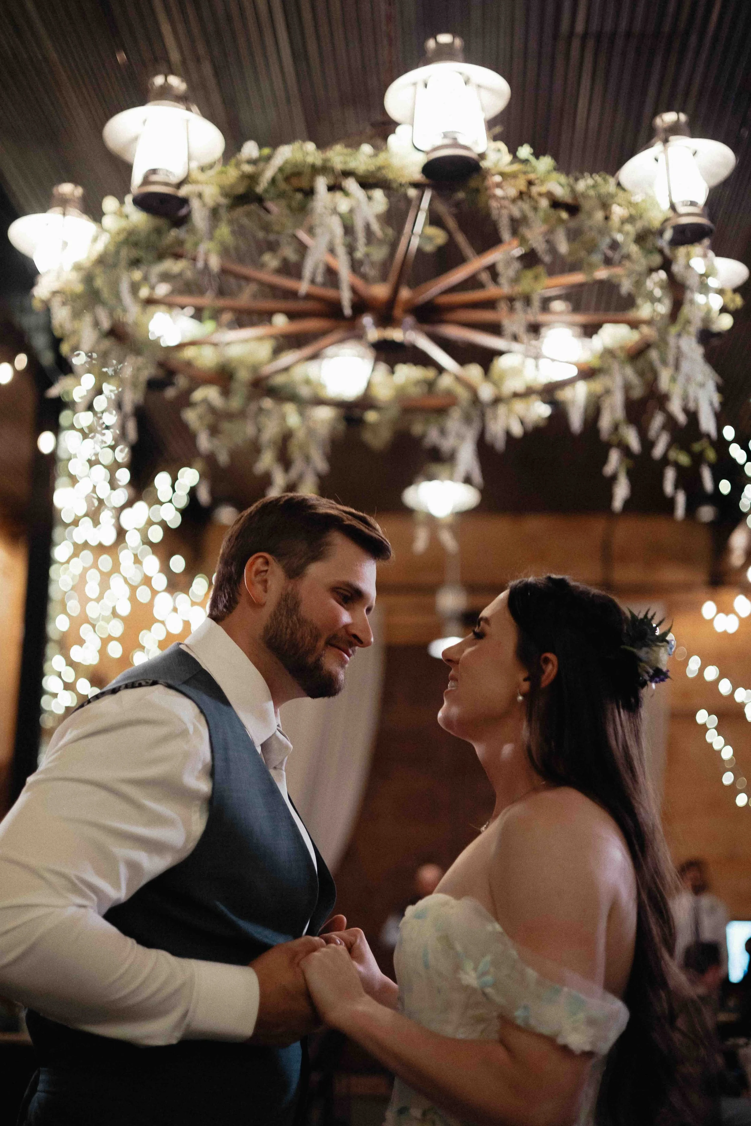Bride and groom dancing in front of twinkling lights and a lit up chandelier in the background.