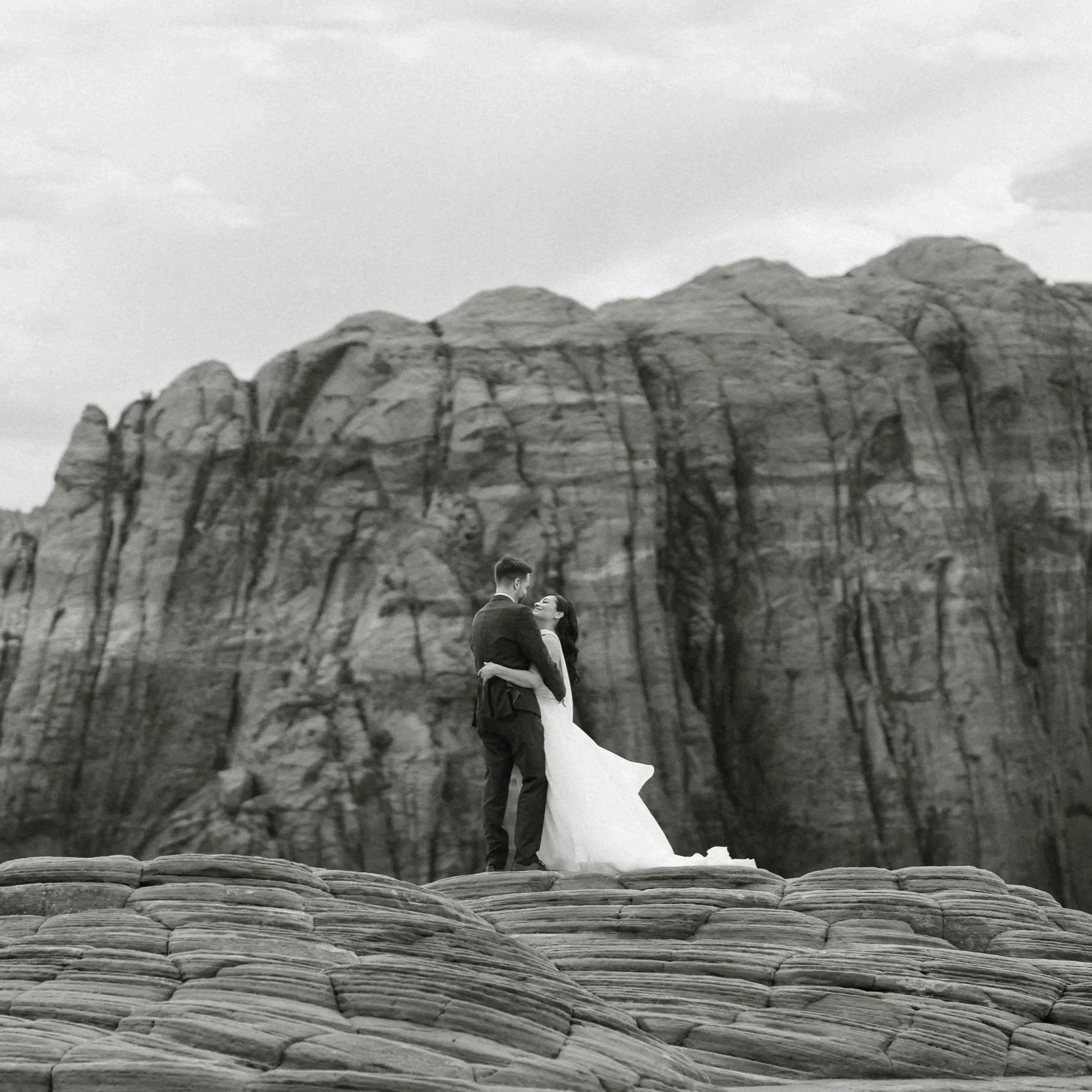 A bride and groom standing atop petrified dunes in southern UT with rock formations in the background.
