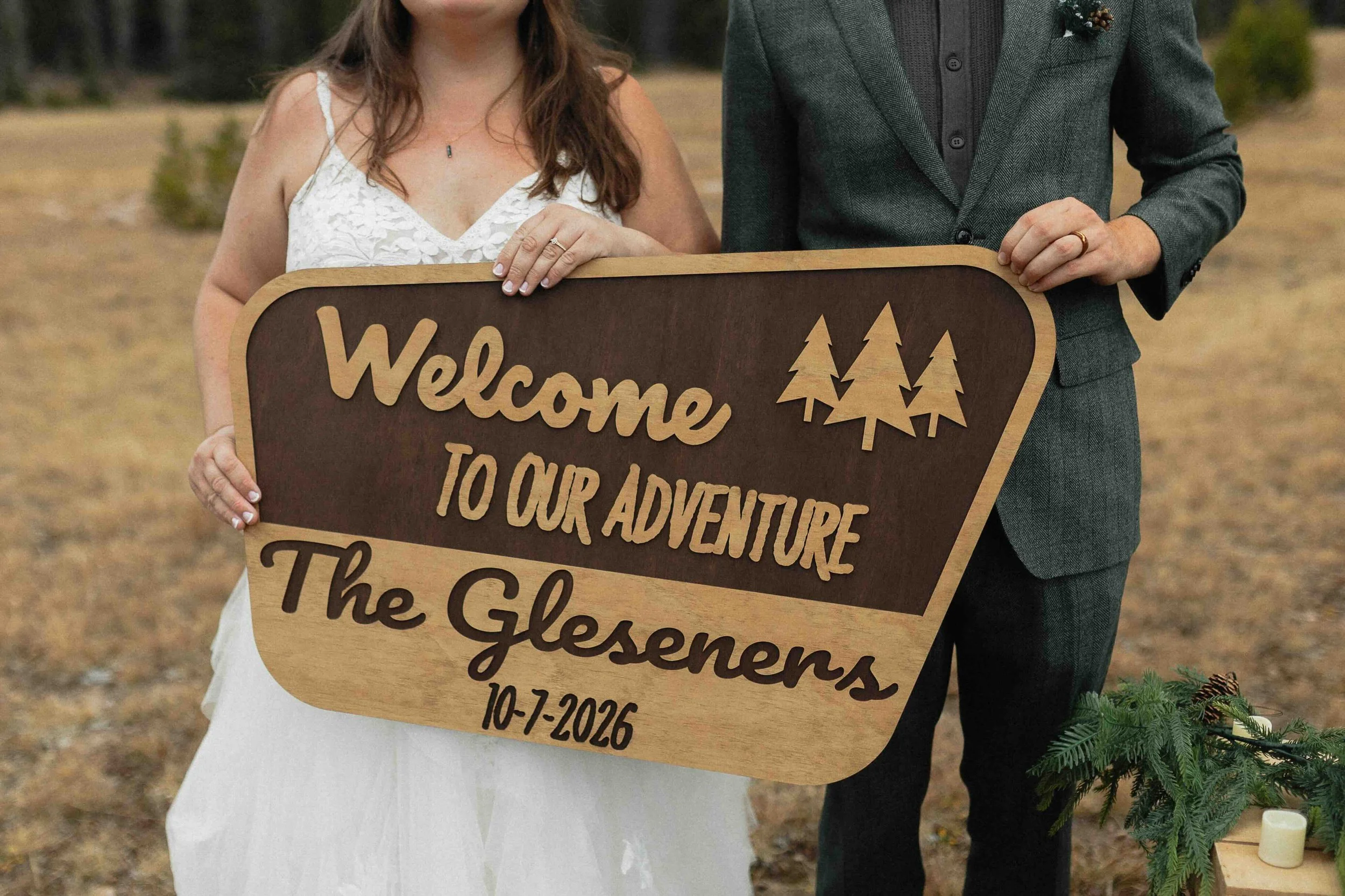 Bride and groom holding a "Welcome to our Adventure" sign with their wedding date on it "10-7-2026."