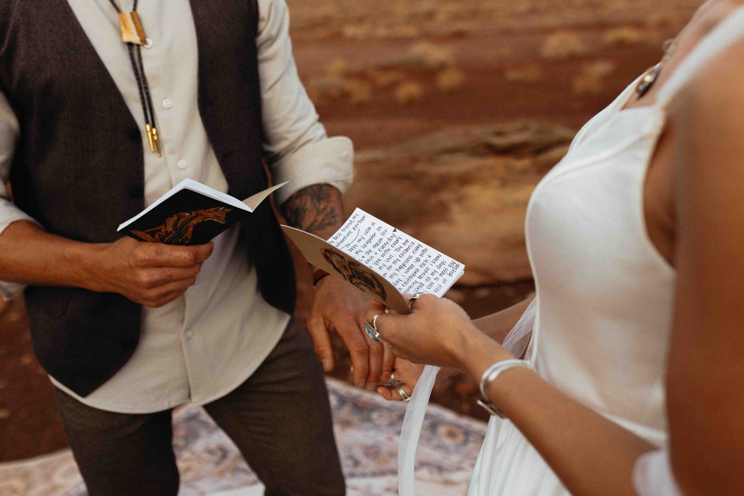 Bride and groom reading vows and holding hands in the desert.
