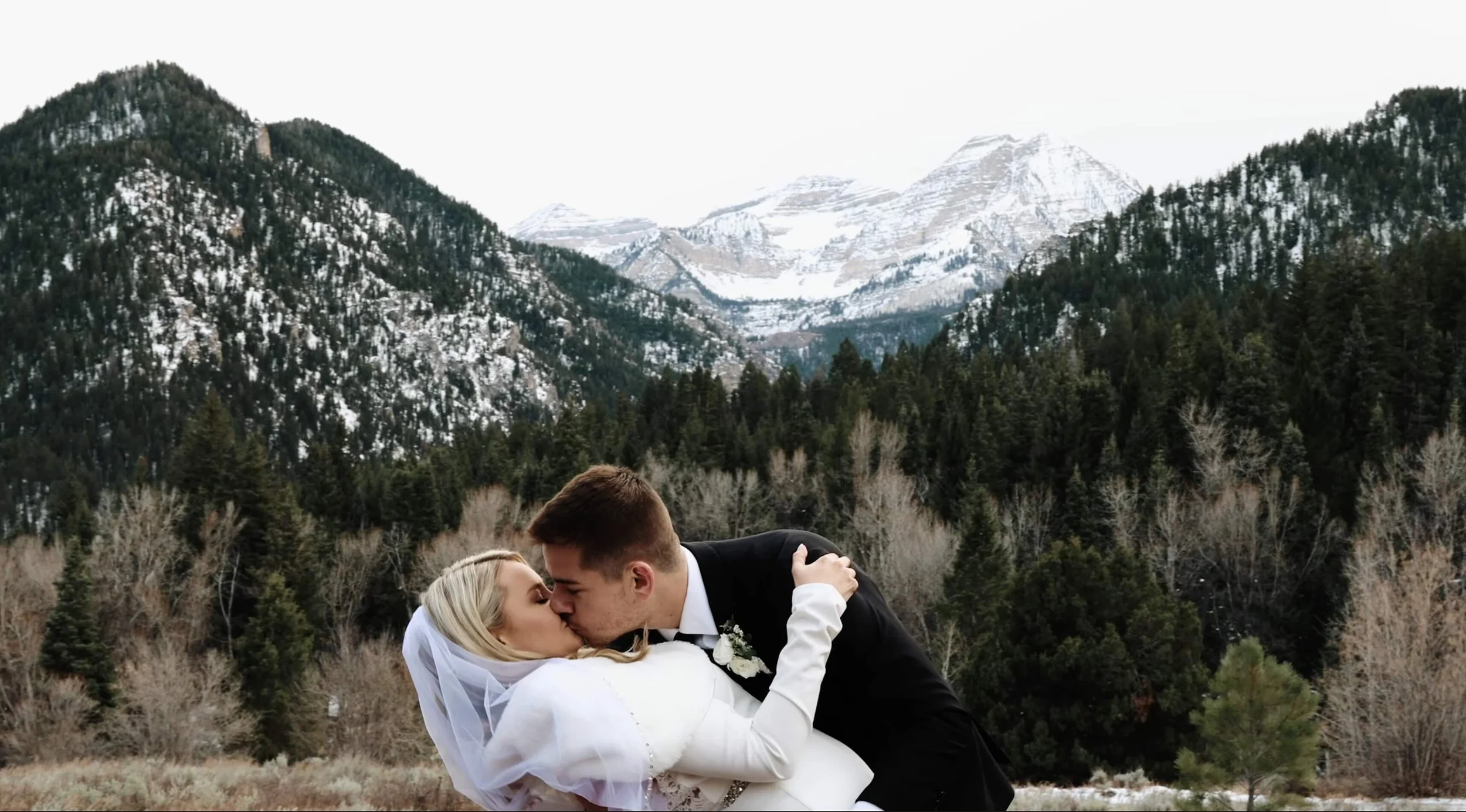 Bridal couple kissing in front of snowy mountains.