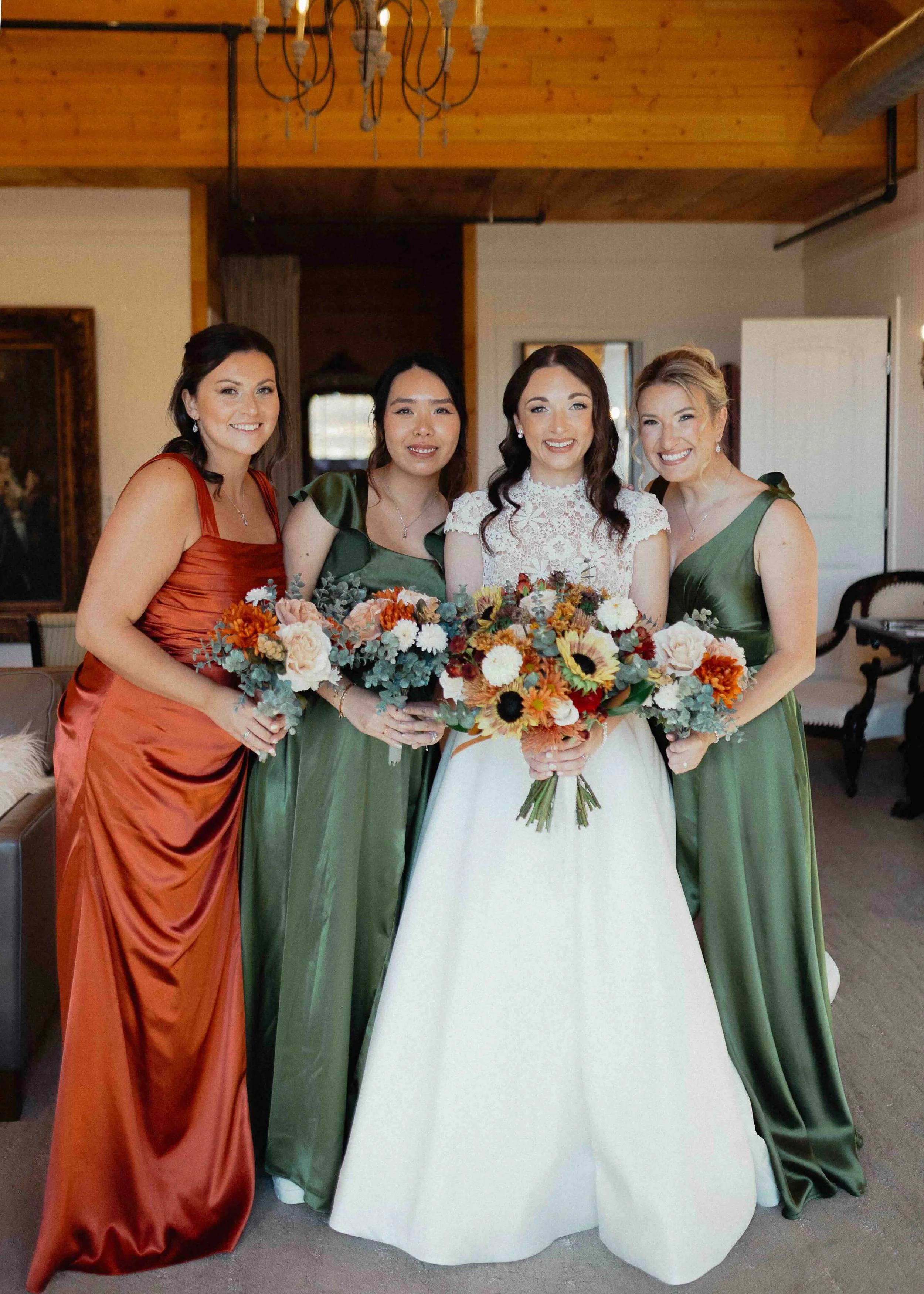 Bride standing with bridesmaids in copper and green dresses, holding onto her bouquet.