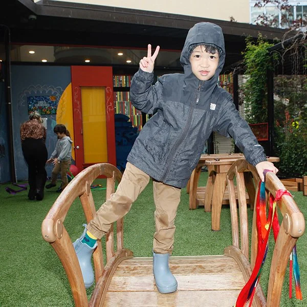 A pre-k student flashes a peace sign while playing in the rain