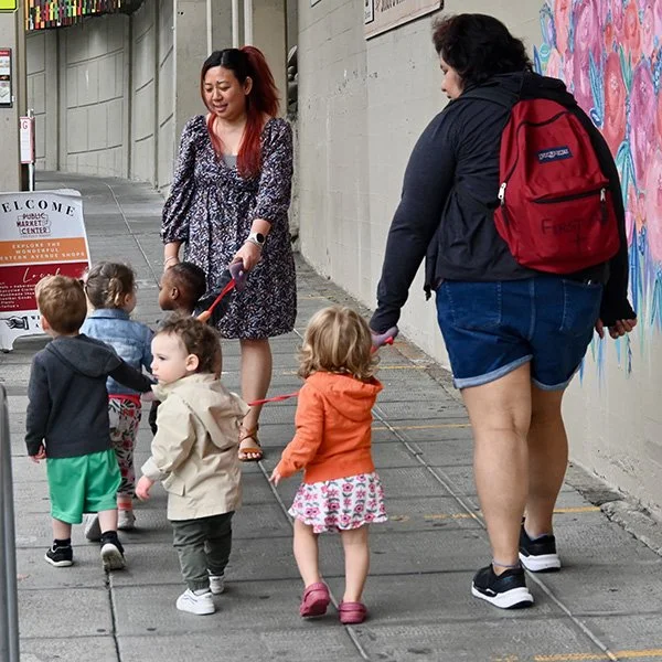 Two teachers guide toddlers on a walk in Pike Place Market
