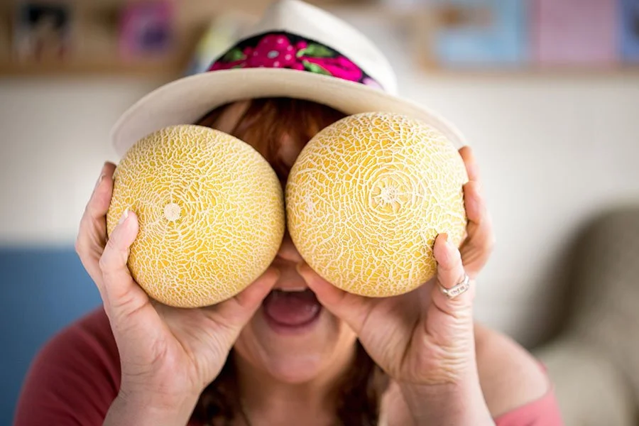 Headshot of Ezelia, Nutrition Coordinator, holding cantaloupes in front of her eyes and being silly