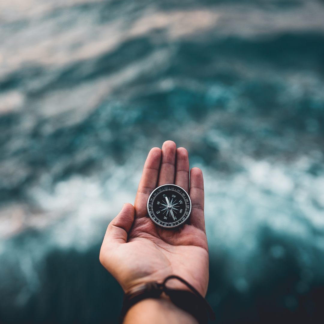 A hand is open holding a compass above a water background.