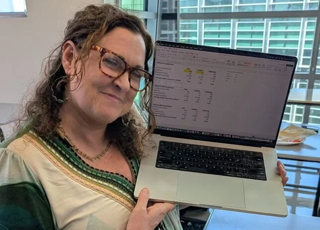 A smiling therapist holding up a laptop with an hours spreadsheet