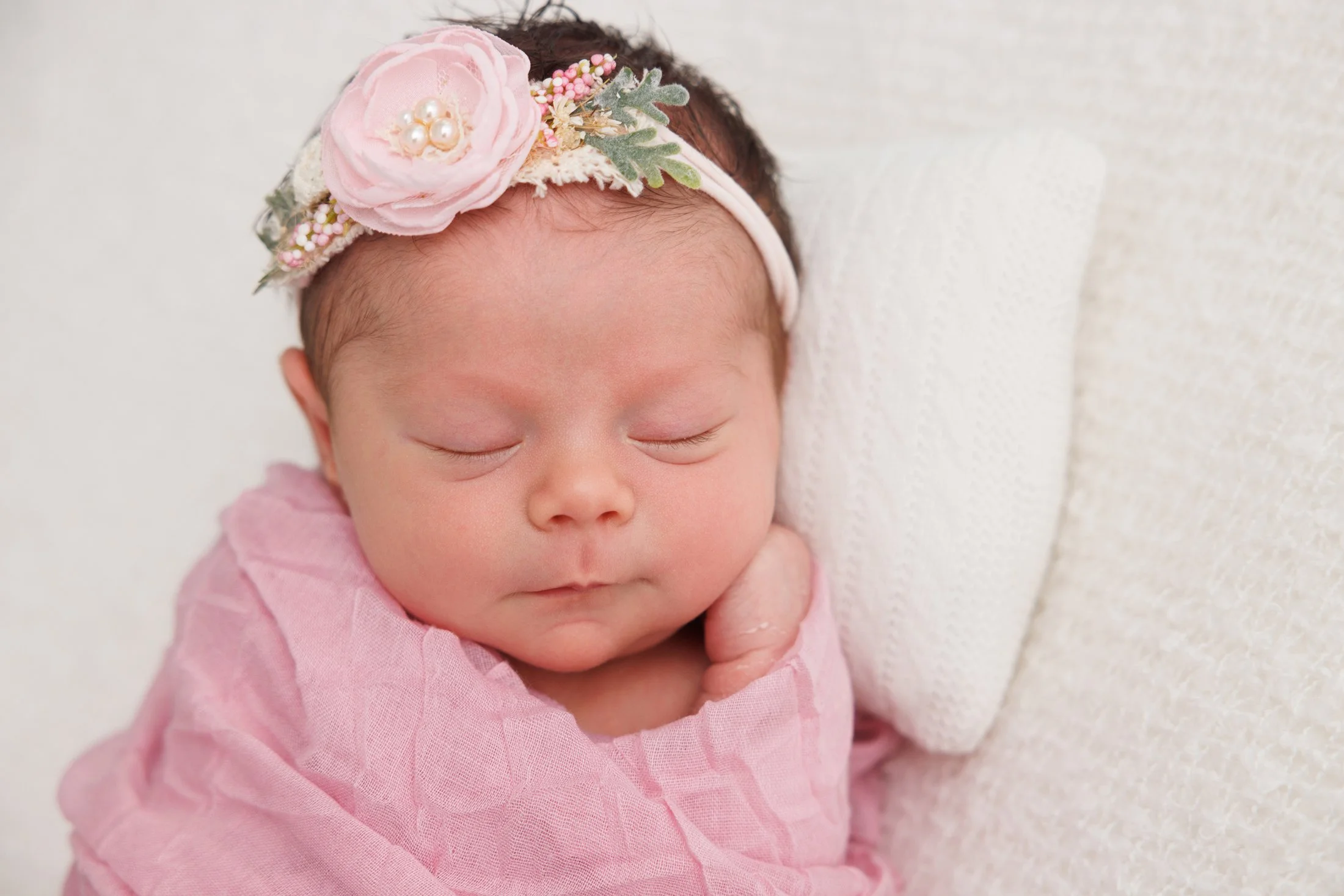 newborn baby girl with pink flower headband in a pink wrap