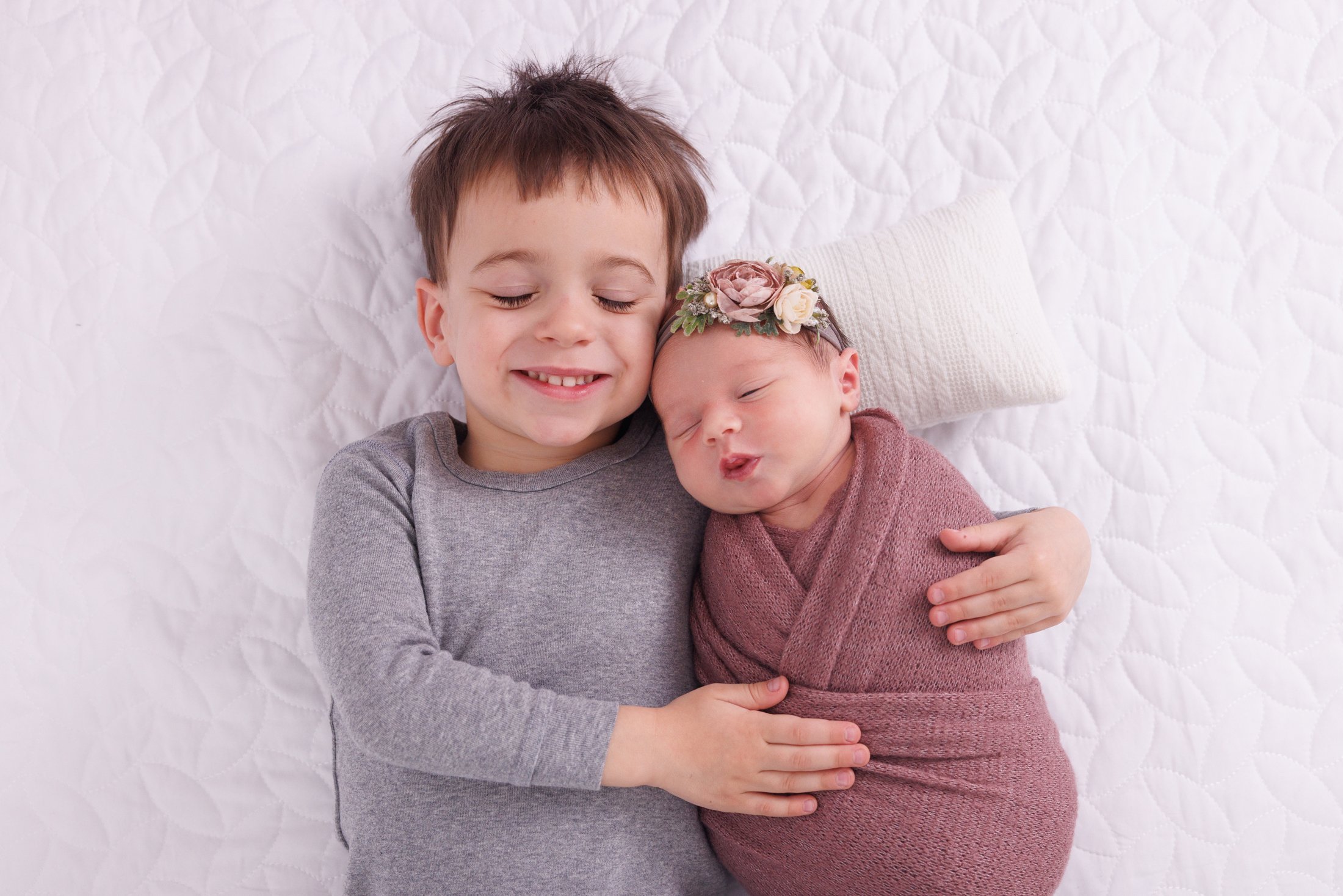 big brother in grey shirt hodling newborn baby sister