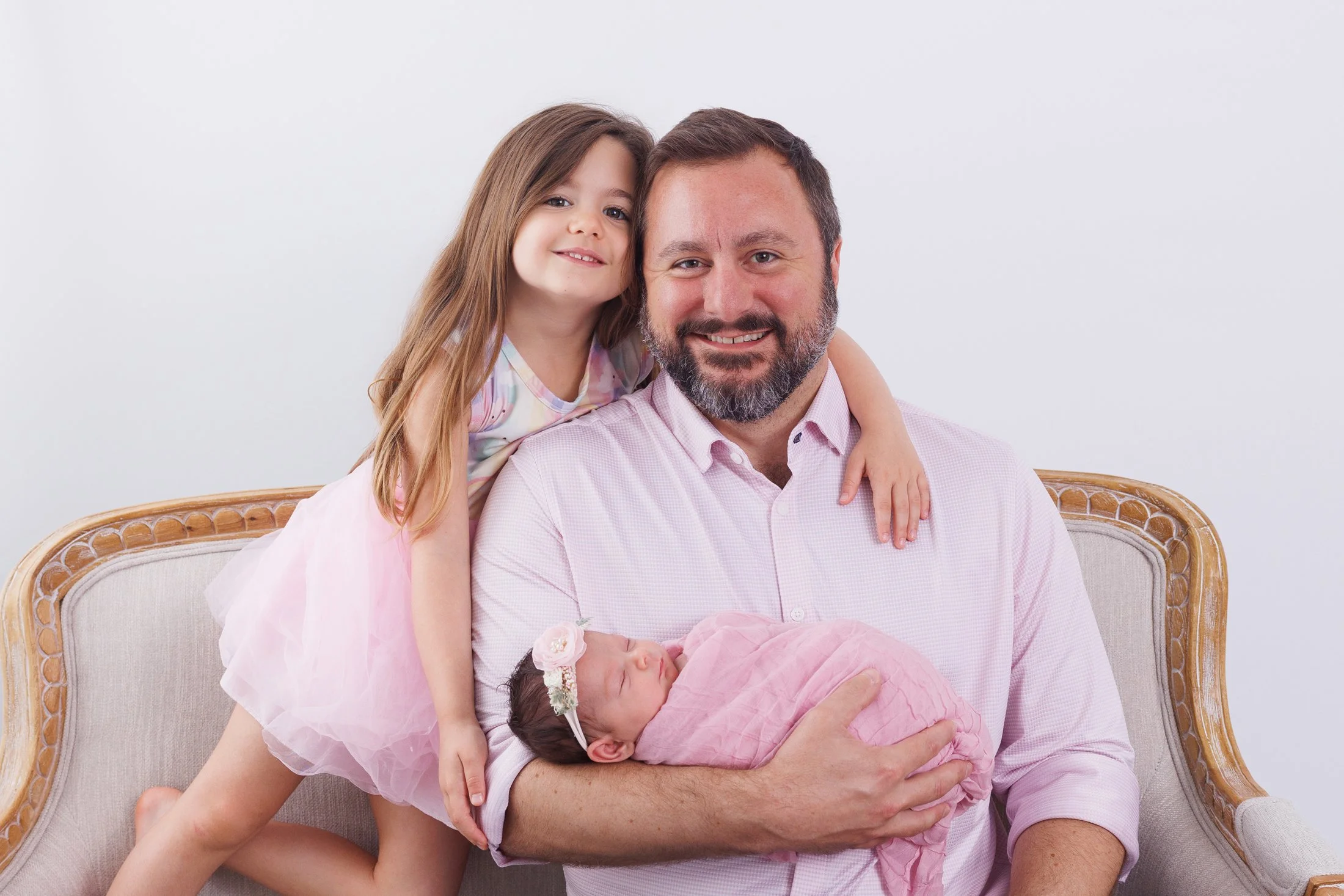 dad on couch holding newborn and older daughter