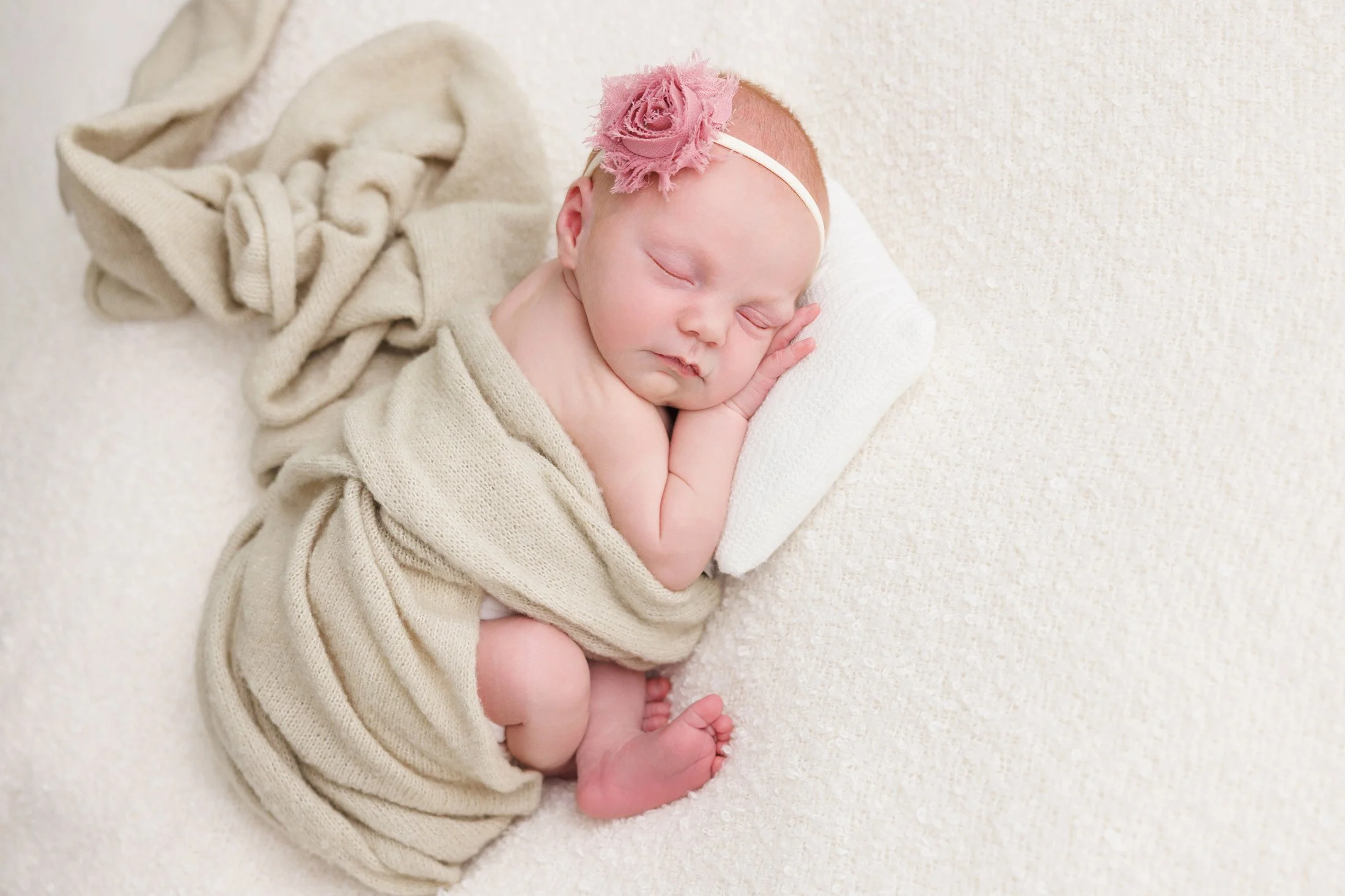 newborn on a white blanket in green wrap