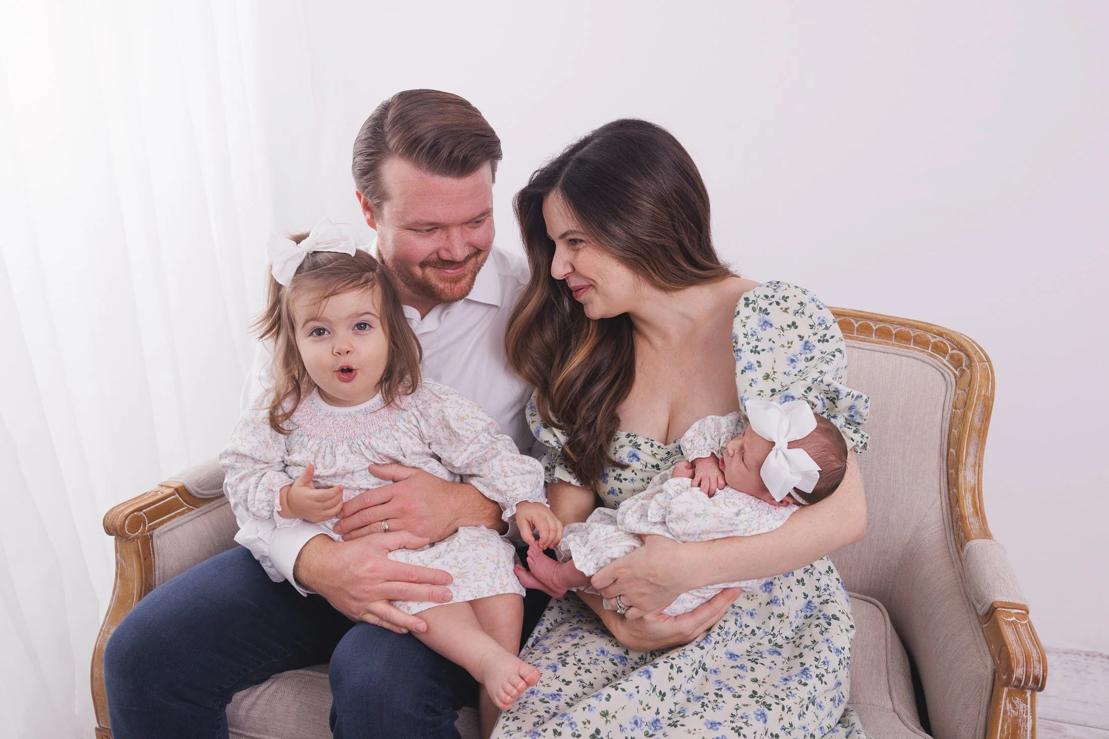 family of 4 with newborn baby and toddler girl sitting on a couch